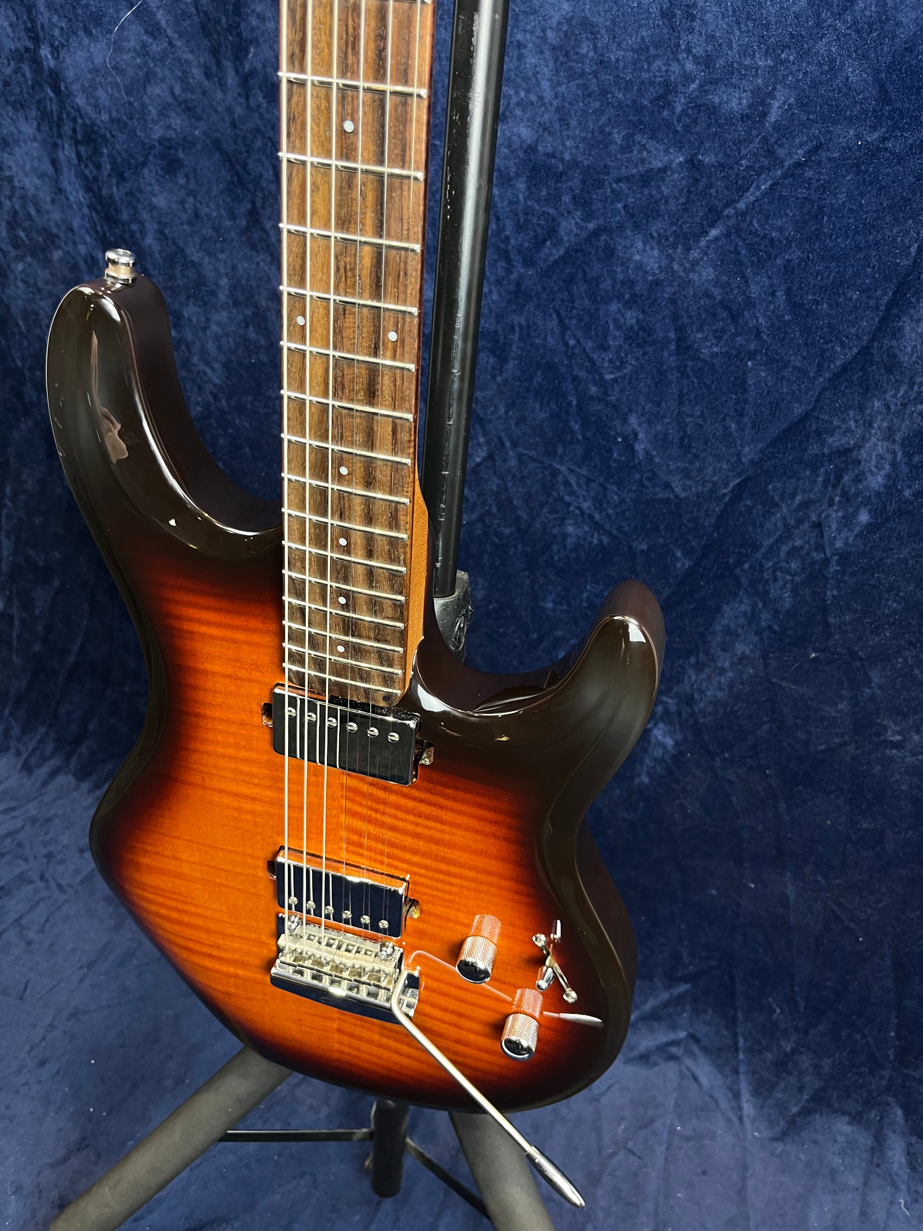 Sunburst electric guitar with two humbucker pickups, a tremolo bridge, two control knobs, and a switch, standing on a black tripod stand.