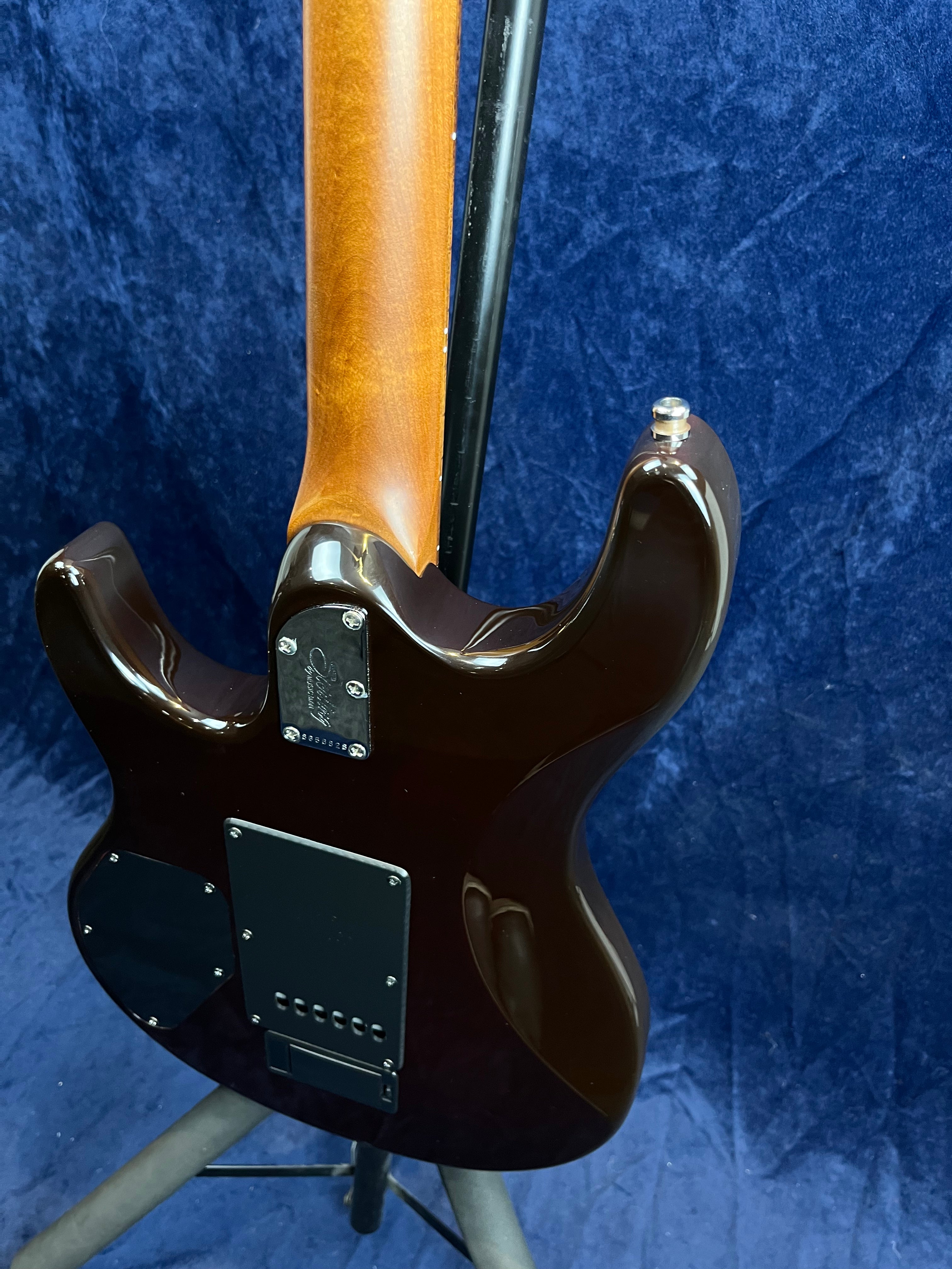 Back view of an electric guitar showing a glossy dark brown body, natural wood neck, and black back plates, set against a deep blue background.