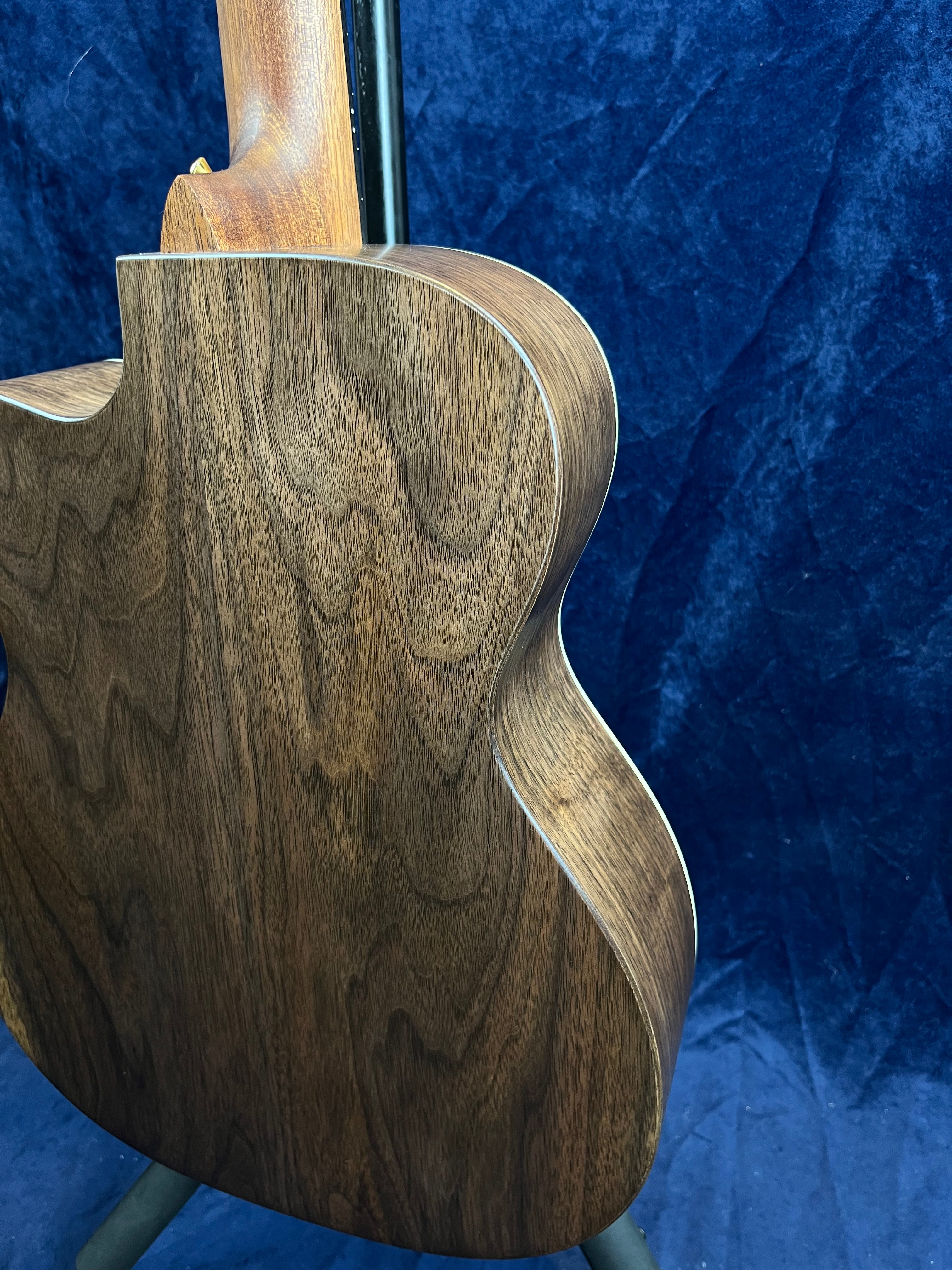 Back side of a Martin acoustic guitar showing dark wood grain with a smooth, rounded shape and light binding along the edges.