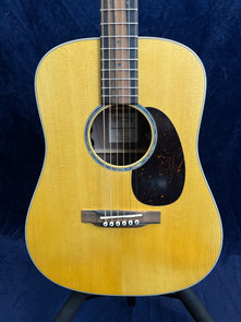 Martin acoustic guitar with a natural wood finish, dark wood bridge, six white bridge pins, and a black pickguard on the right side of the sound hole.