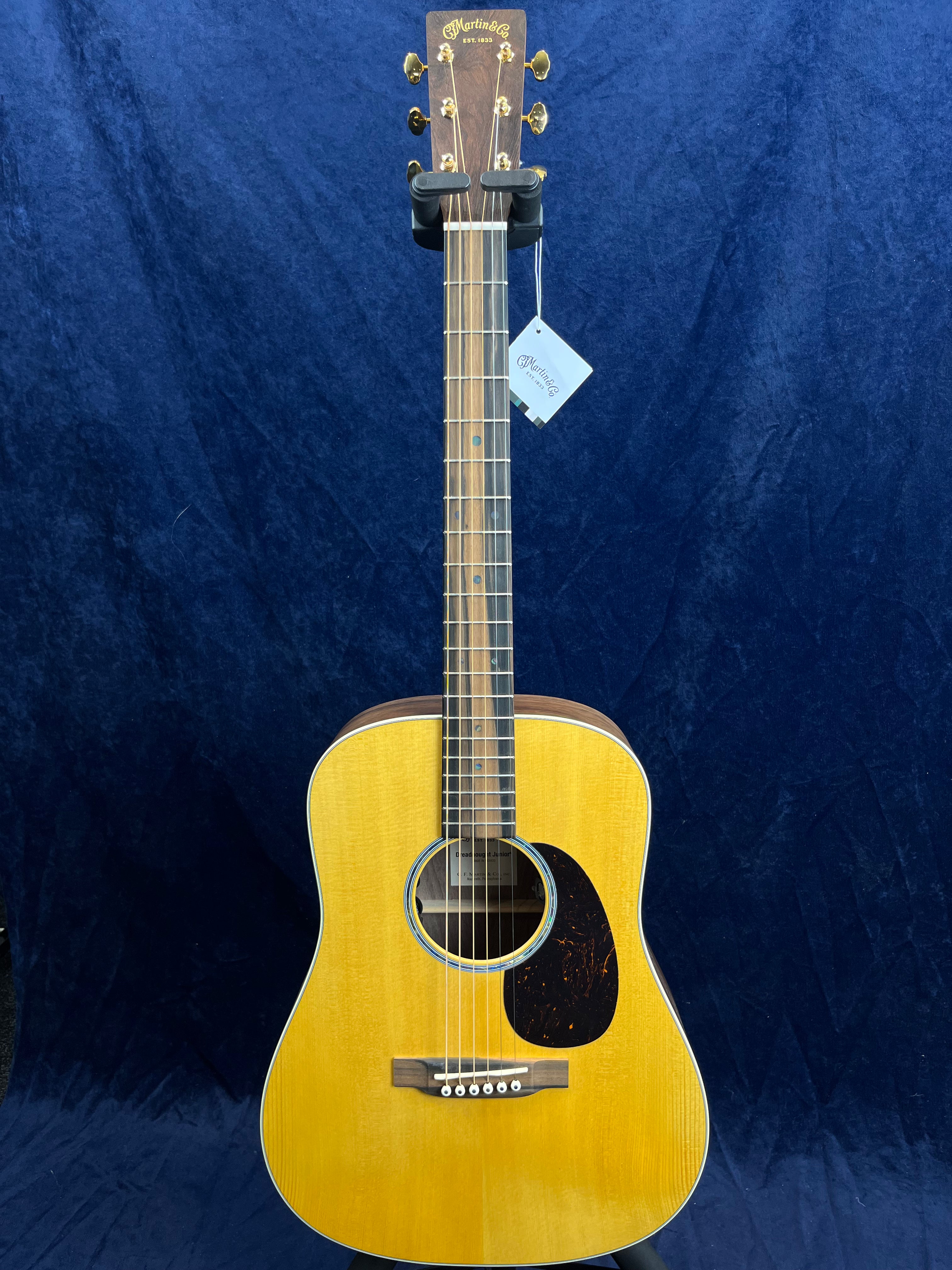 Martin acoustic guitar with a natural wood finish, dark pickguard, and gold tuning pegs, displayed upright against a dark blue background.
