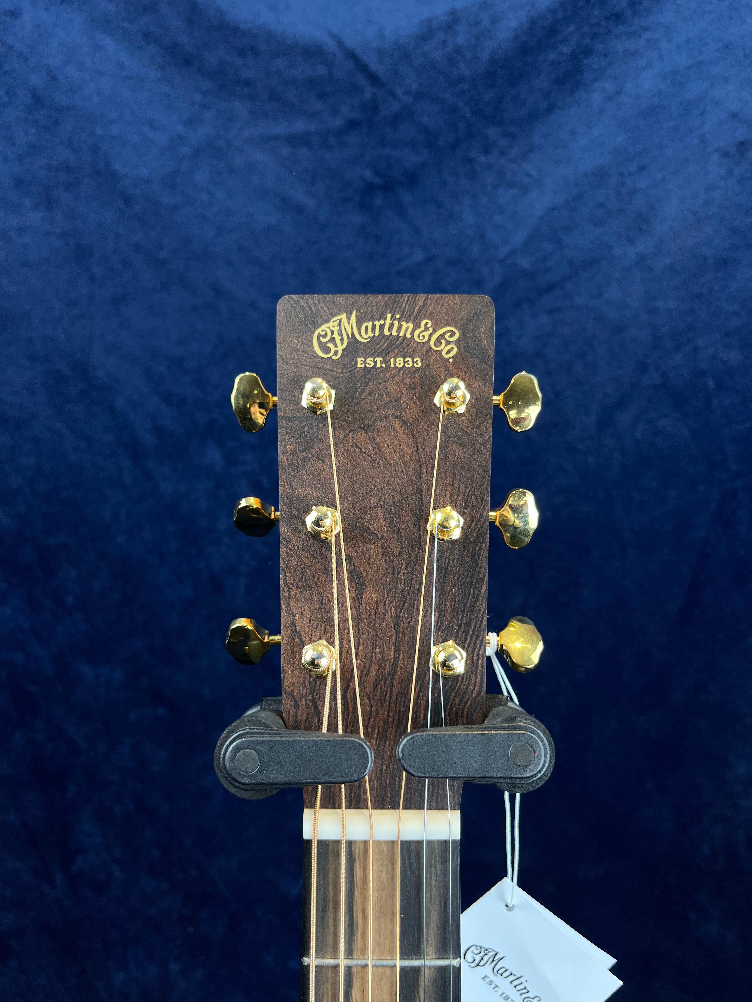 C. F. Martin & Co. acoustic guitar headstock with gold tuning pegs and attached tag, set against a dark blue background.