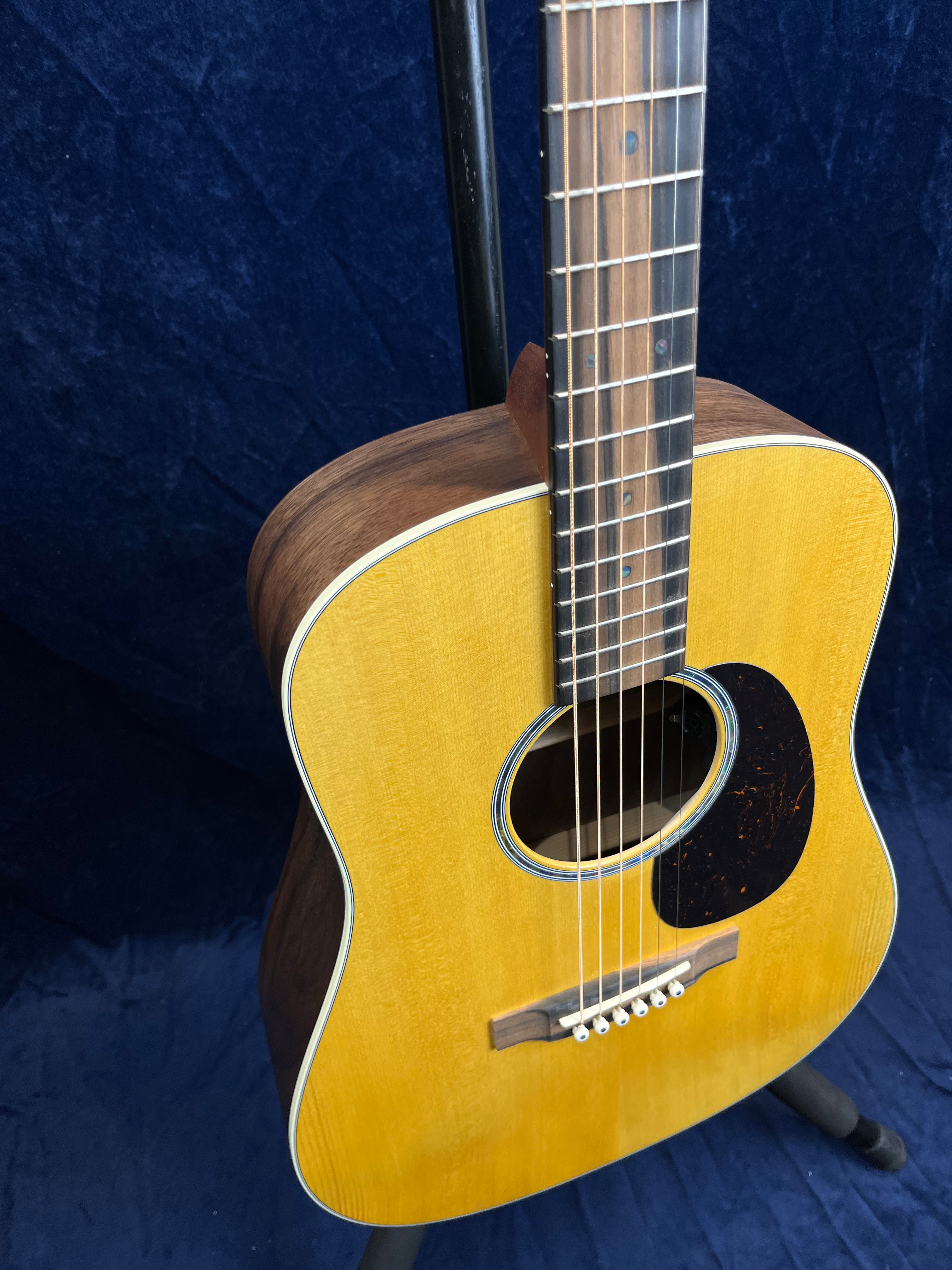 Martin acoustic guitar with a natural wood finish, dark wood sides, white binding, and a black pickguard against a dark blue background.