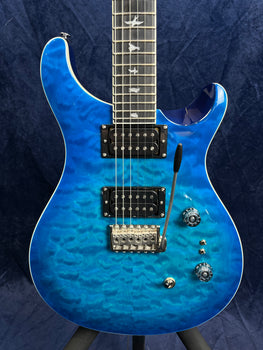 Electric guitar with a bright blue quilted maple top, two humbucker pickups, tremolo bridge, two knobs, two switches, and bird inlays on the fretboard.