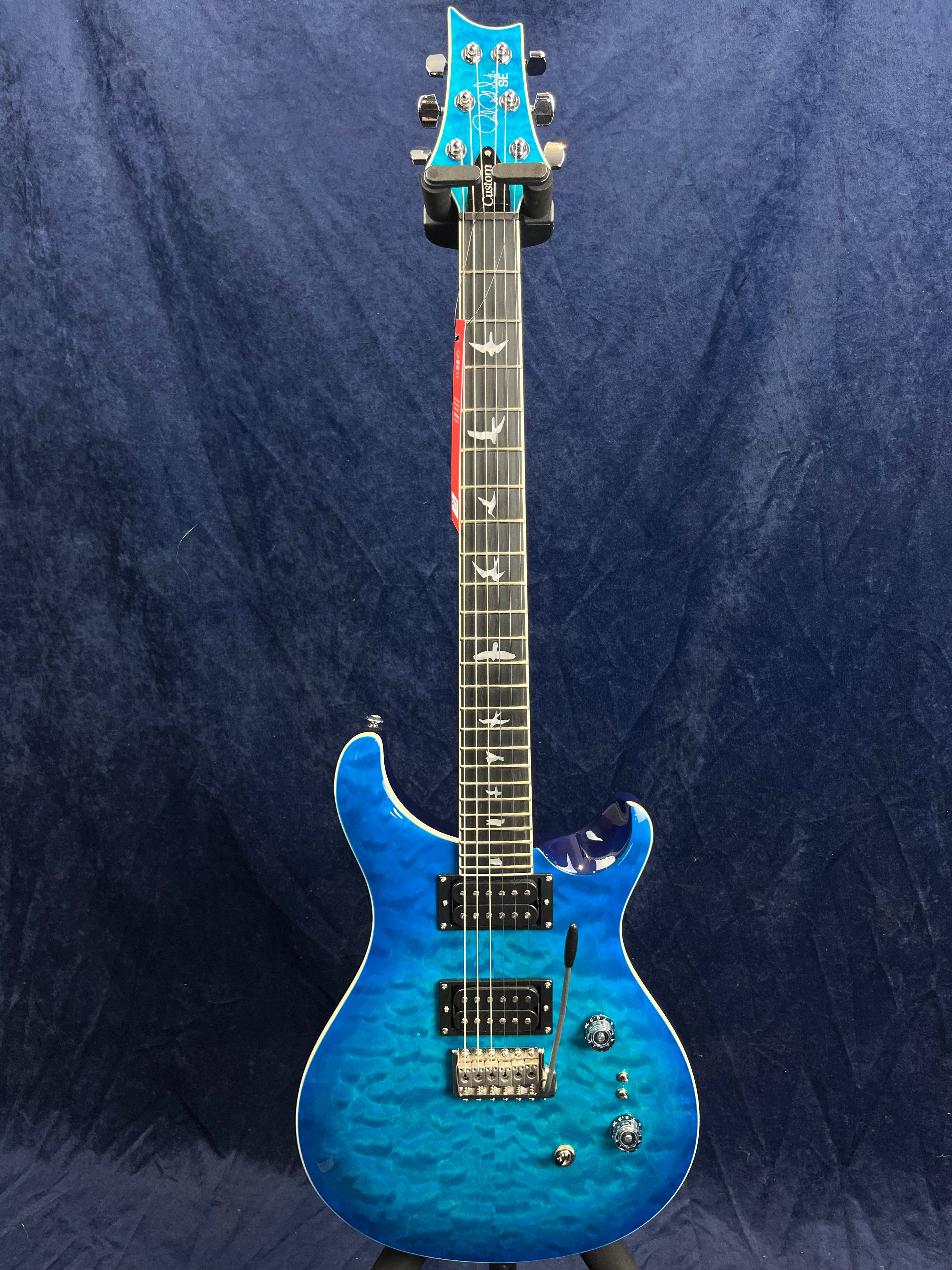 Blue electric guitar with a quilted maple finish, two humbucker pickups, bird inlays on the fretboard, and a whammy bar.