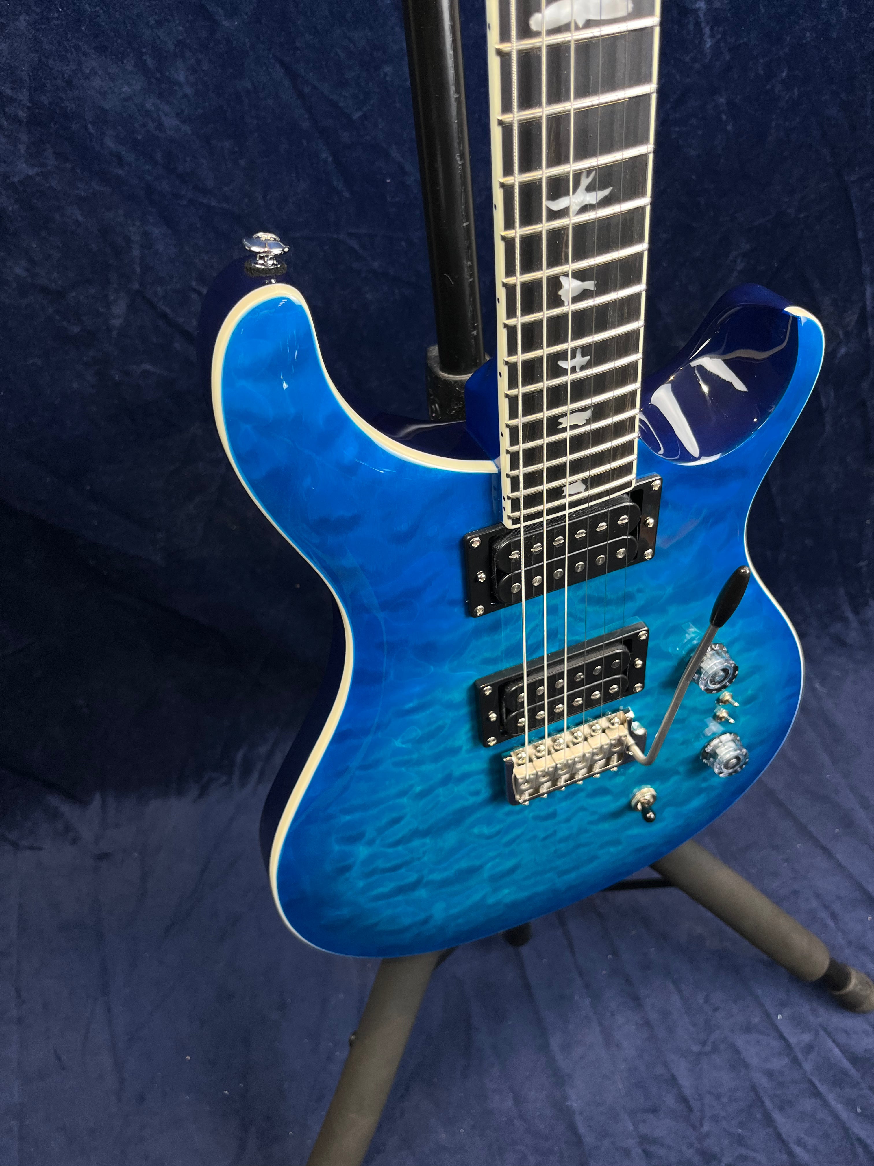 Blue electric guitar with quilted maple top, dual humbucker pickups, three control knobs, and bird-shaped fretboard inlays.