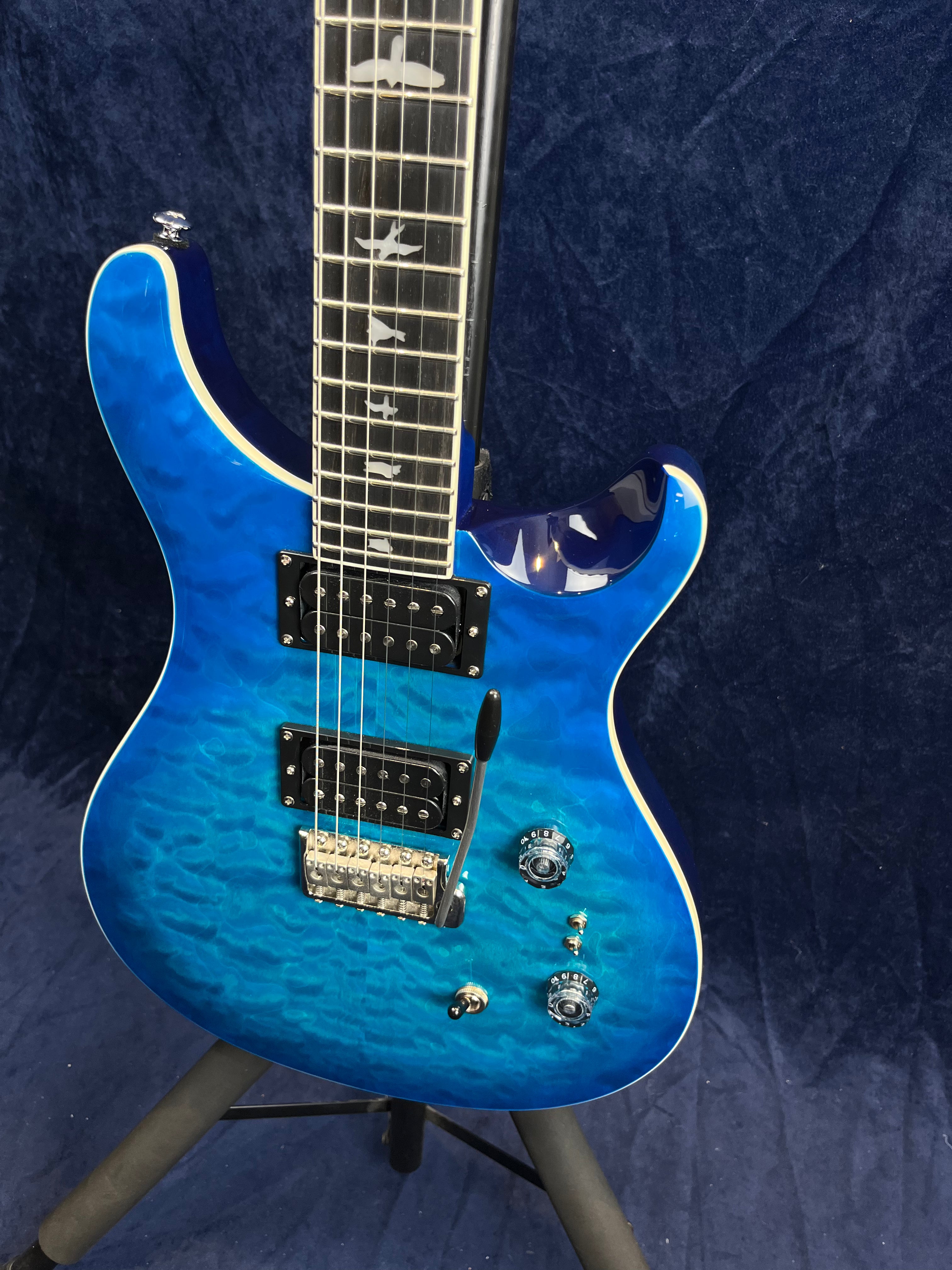 Guitare électrique bleu vif avec table ondulée, deux micros doubles noirs et repères en forme d’oiseaux sur la touche.