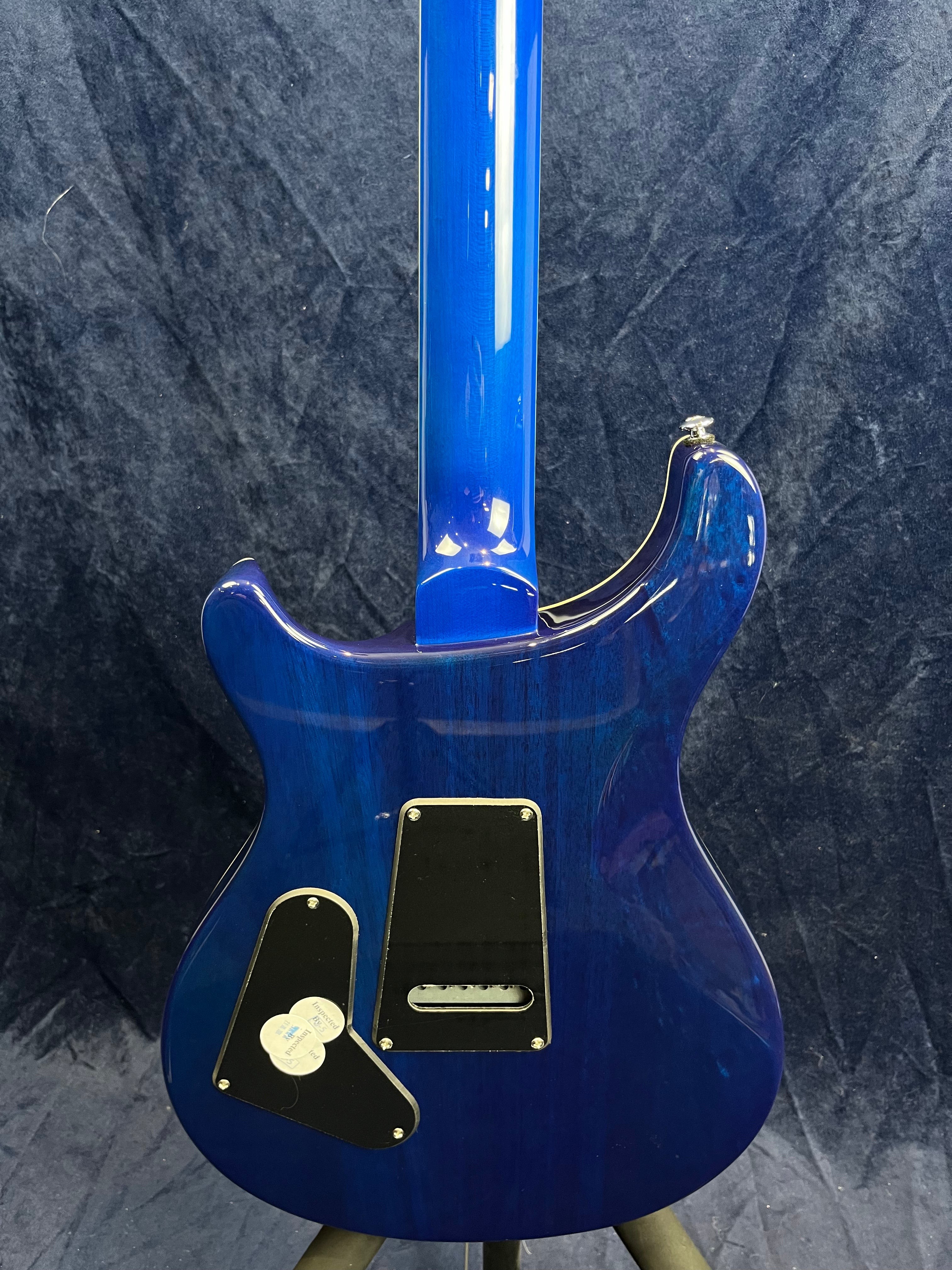 Blue electric guitar viewed from the back, showing a glossy finish and two black plastic cavity covers with screws on the body.