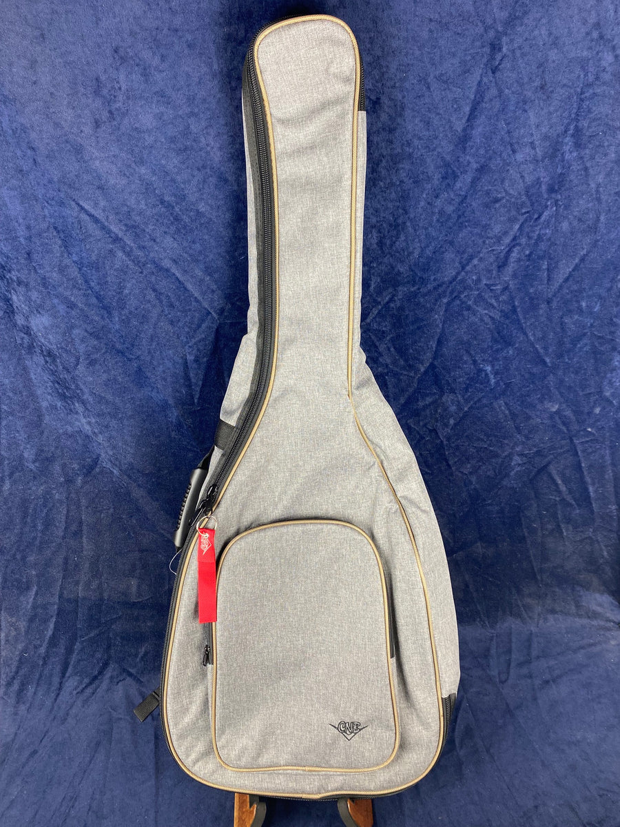 A light gray soft acoustic guitar case with tan trim, front zippered pocket, and a red keychain tag, standing upright against a dark blue background.