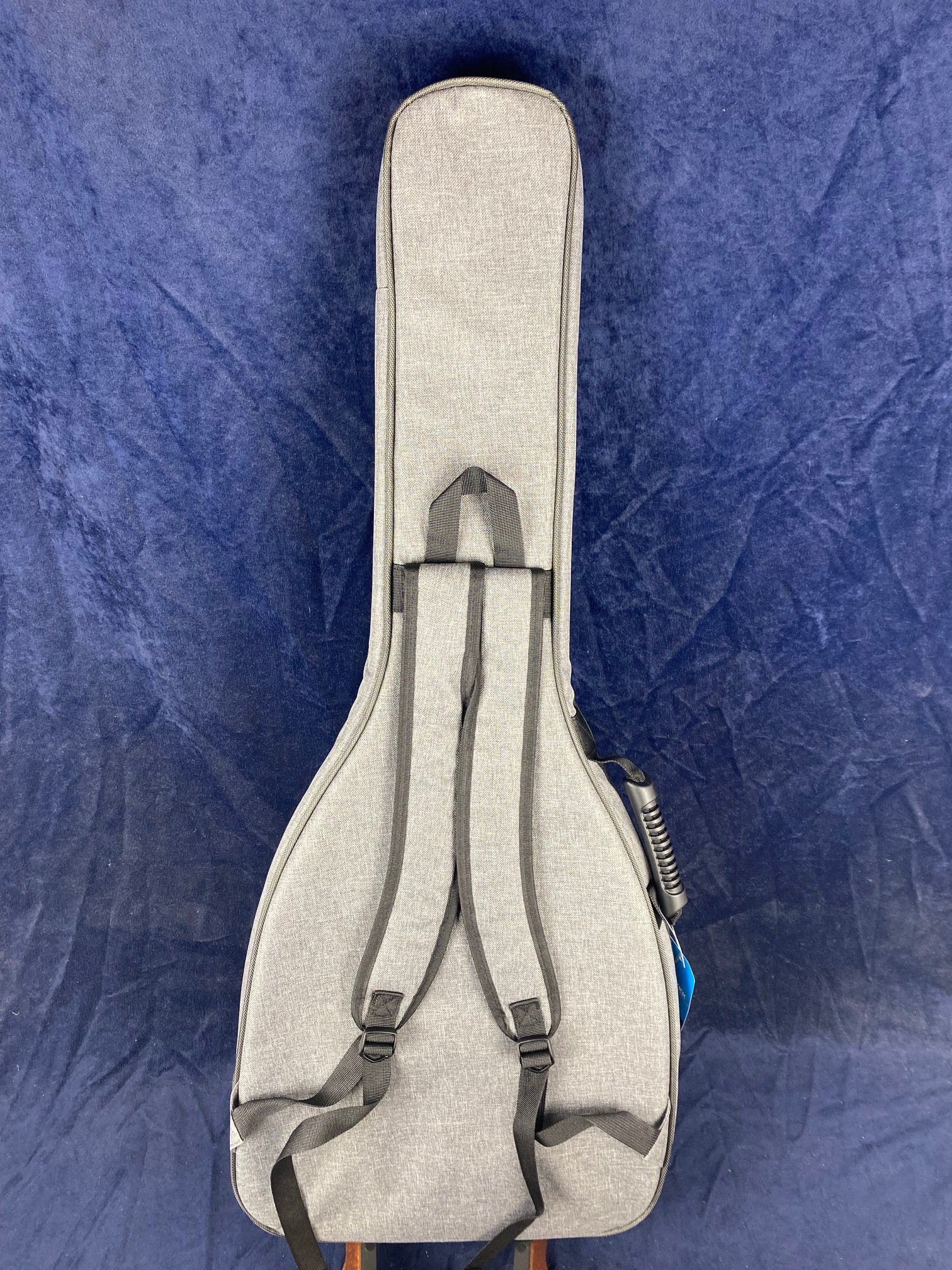 Light gray soft guitar case with two adjustable backpack-style straps, shown against a deep blue background. Electric guitar type.