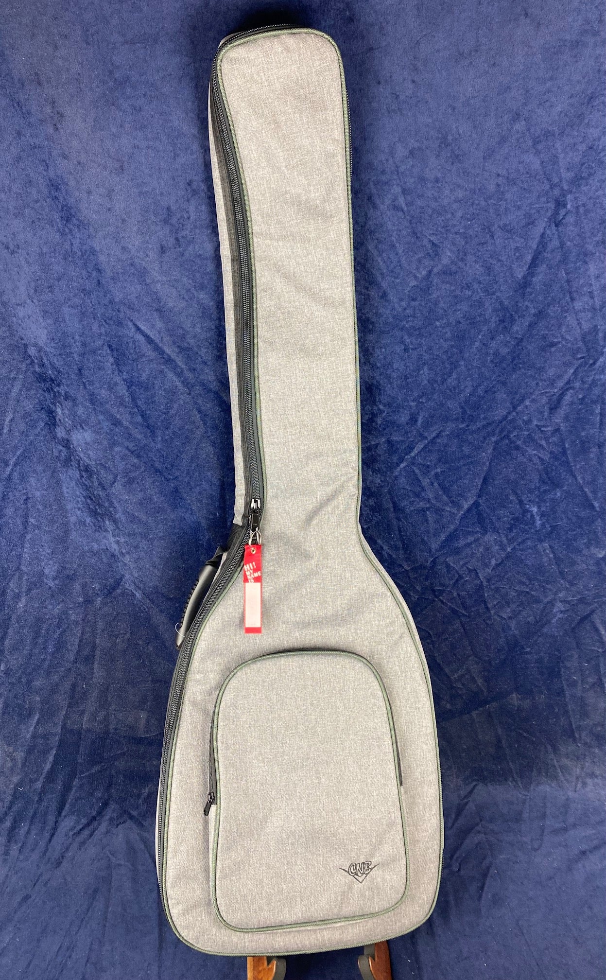 Light gray fabric gig bag for a string instrument, with a front zippered pocket and side handle, resting on a dark blue background.