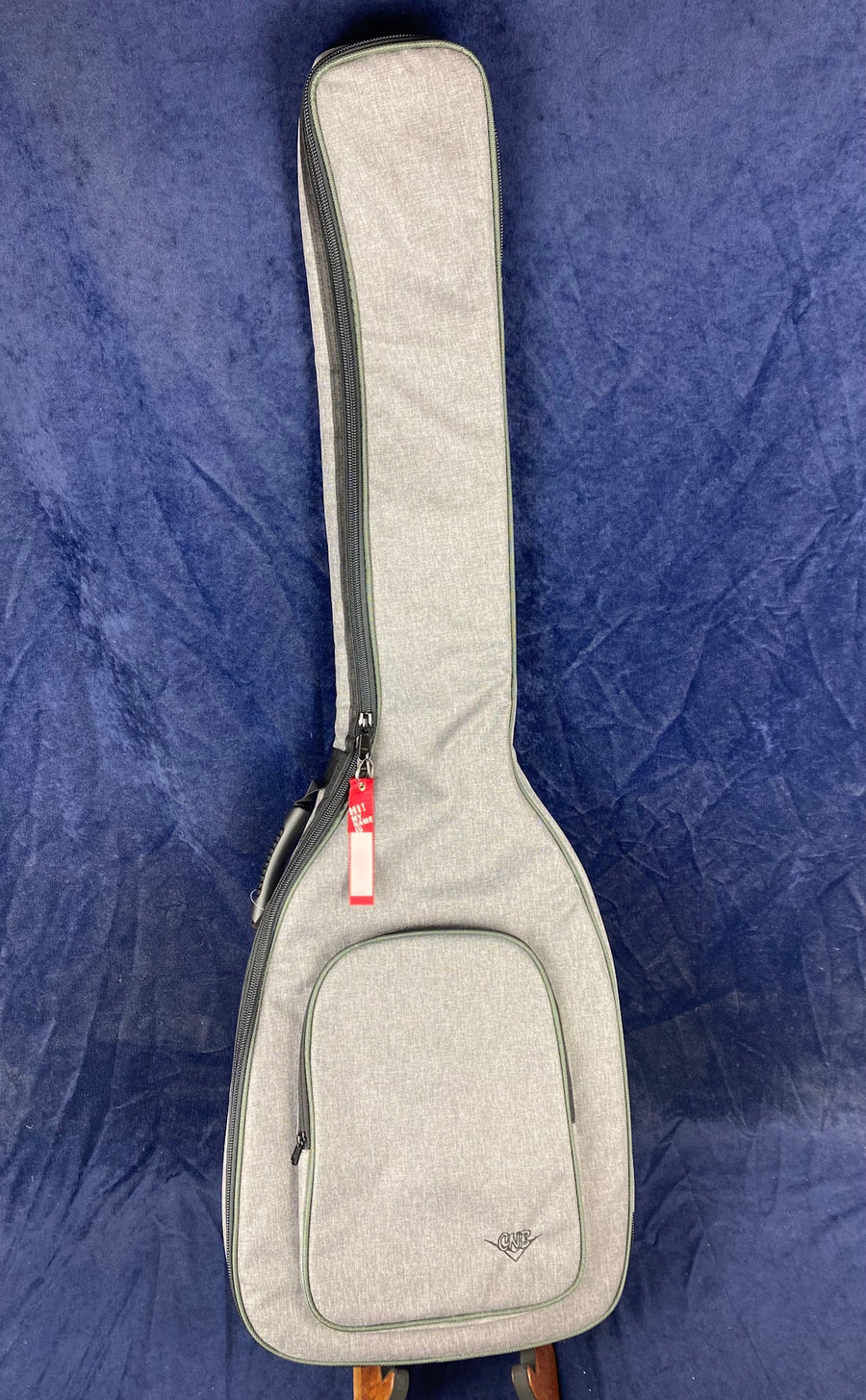 Light gray fabric gig bag for a string instrument, with a front zippered pocket and side handle, resting on a dark blue background.