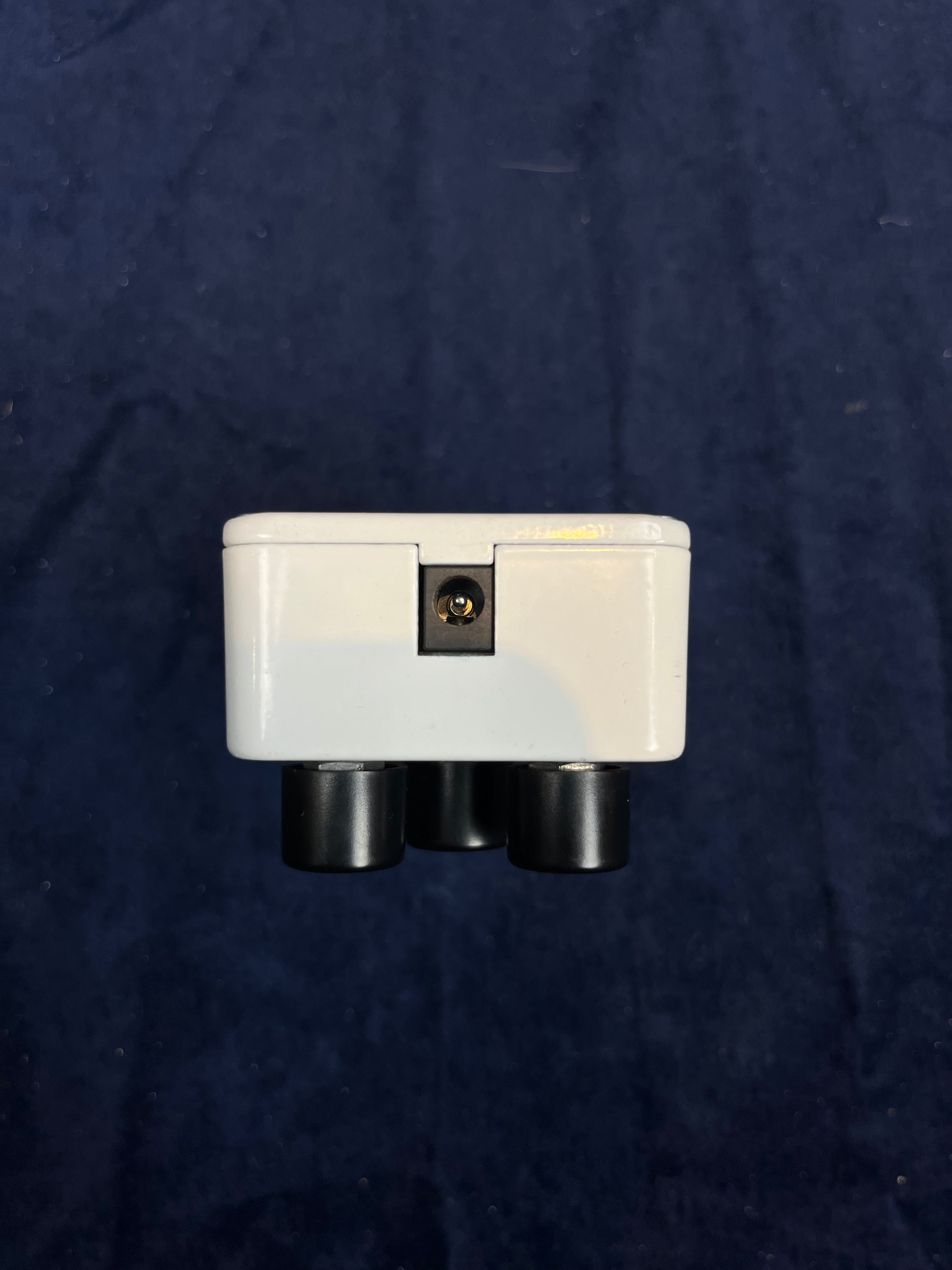 White FX pedal viewed from the side, showing a single power input jack in the center and three black knob bases along the bottom edge.