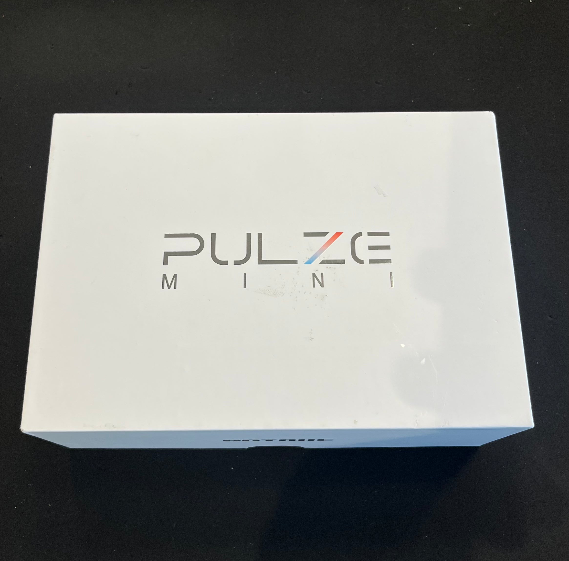 White rectangular box labeled "PULZE MINI" contains an amplifier, with simple modern lettering and a clean design.