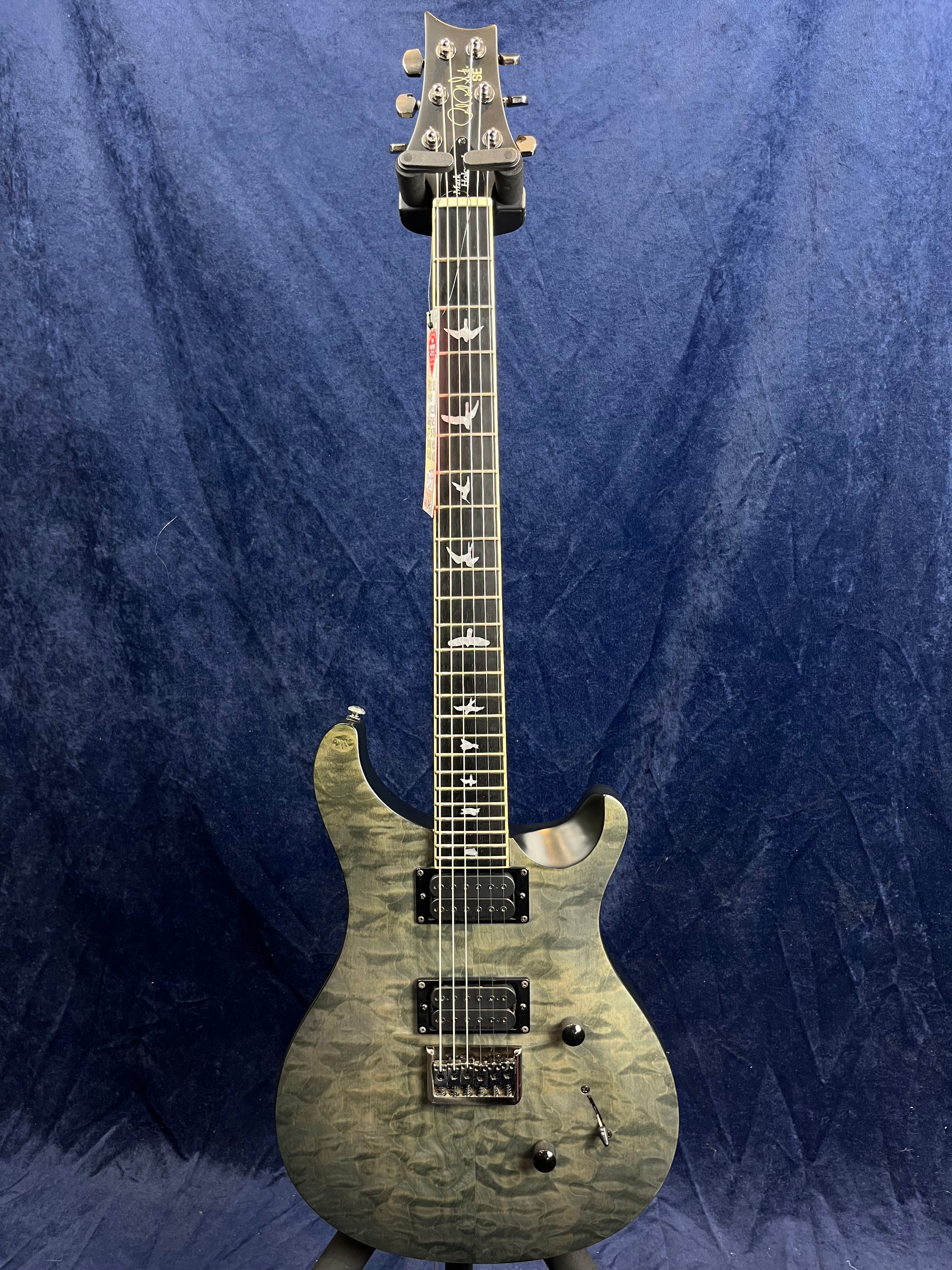 Gray electric guitar with a quilted maple top, bird inlays on the fretboard, two humbucker pickups, and a tremolo bridge, set against a blue background.