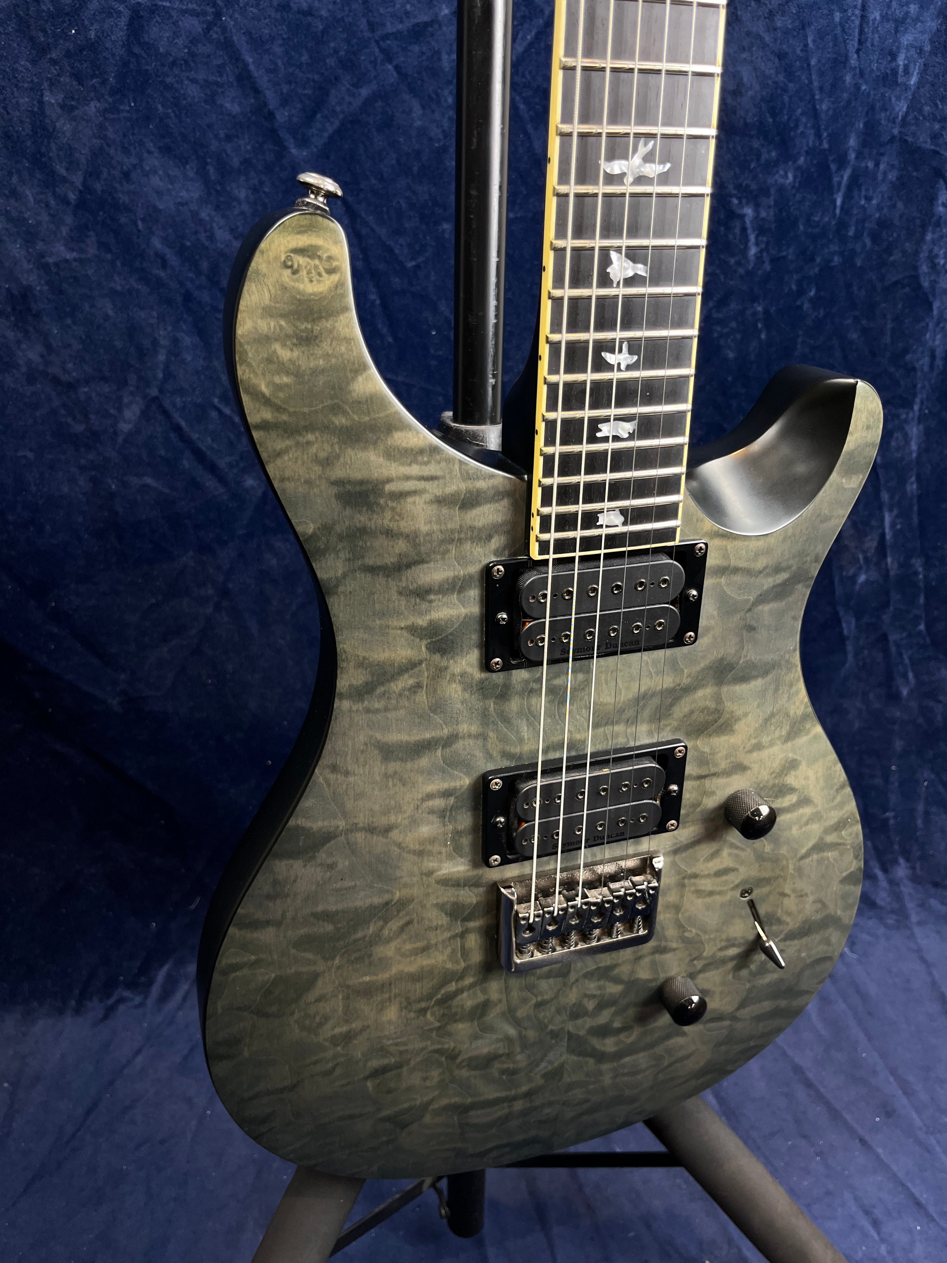 Green quilted maple electric guitar with two black humbucker pickups, bird inlays on the fretboard, and a tremolo bridge.