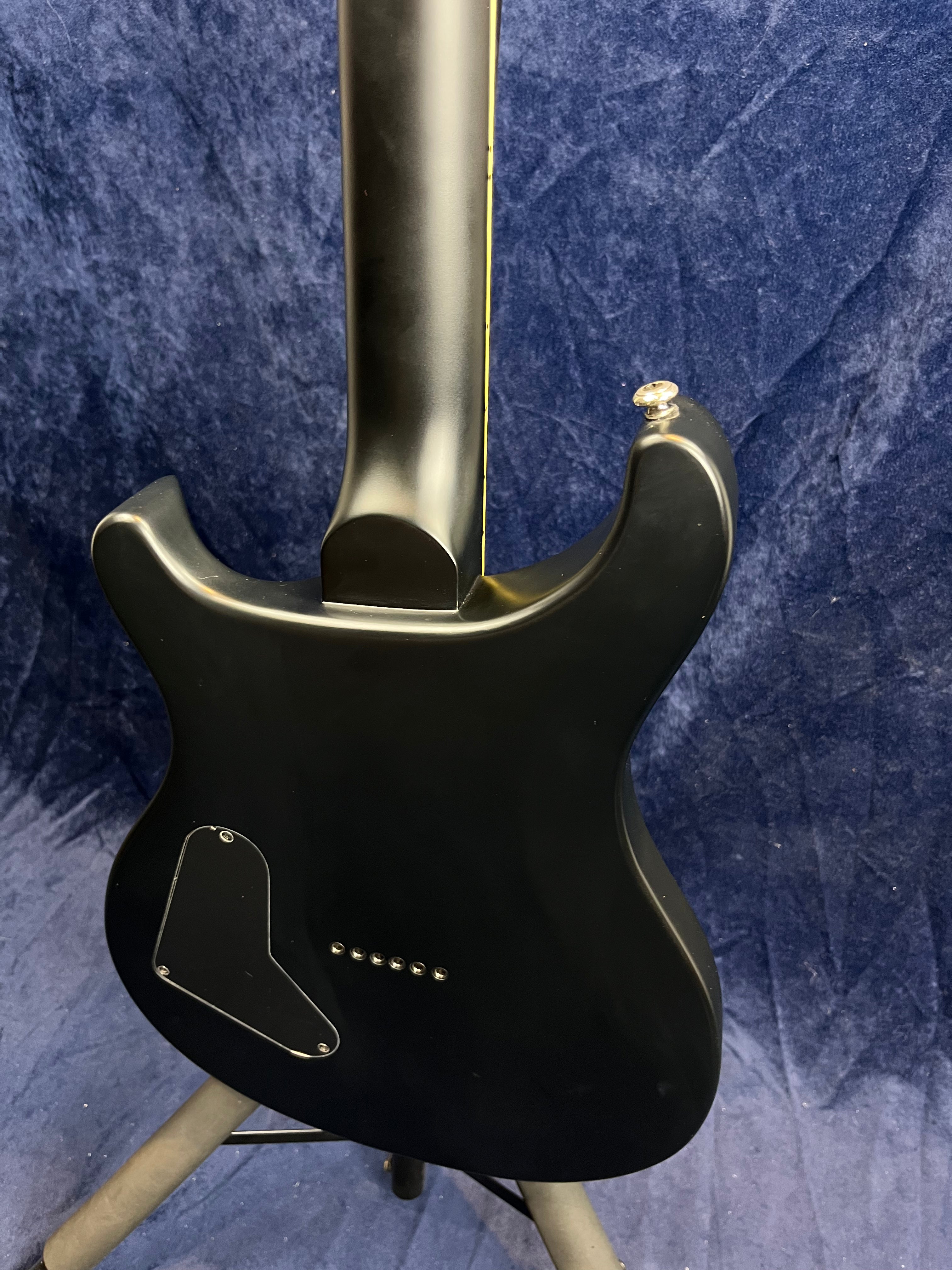 Black electric guitar shown from the back, with a matte finish, rear control plate, and string ferrules for through-body stringing.