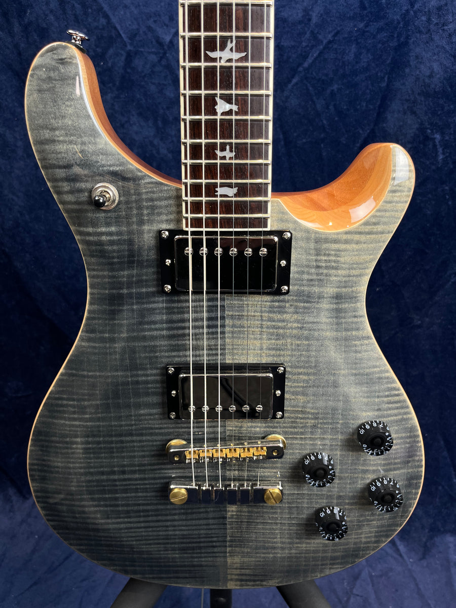Guitare électrique gris foncé avec deux micros doubles noirs, quatre boutons noirs, et repères en forme d’oiseau incrustés sur la touche du manche.