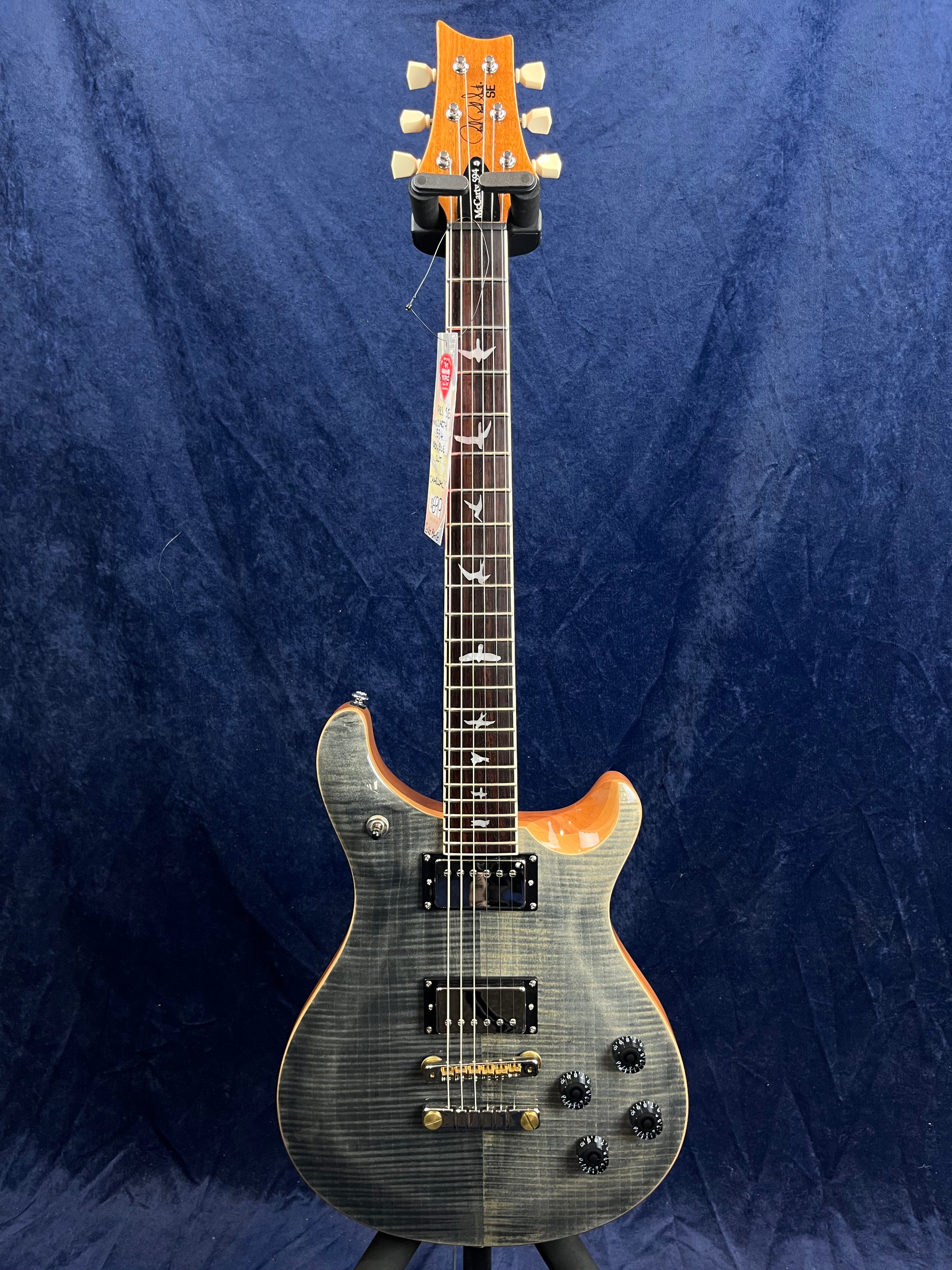 Guitare électrique à corps gris foncé veiné, deux micros doubles noirs, quatre boutons noirs, touche avec incrustations d’oiseaux, tête en bois clair.