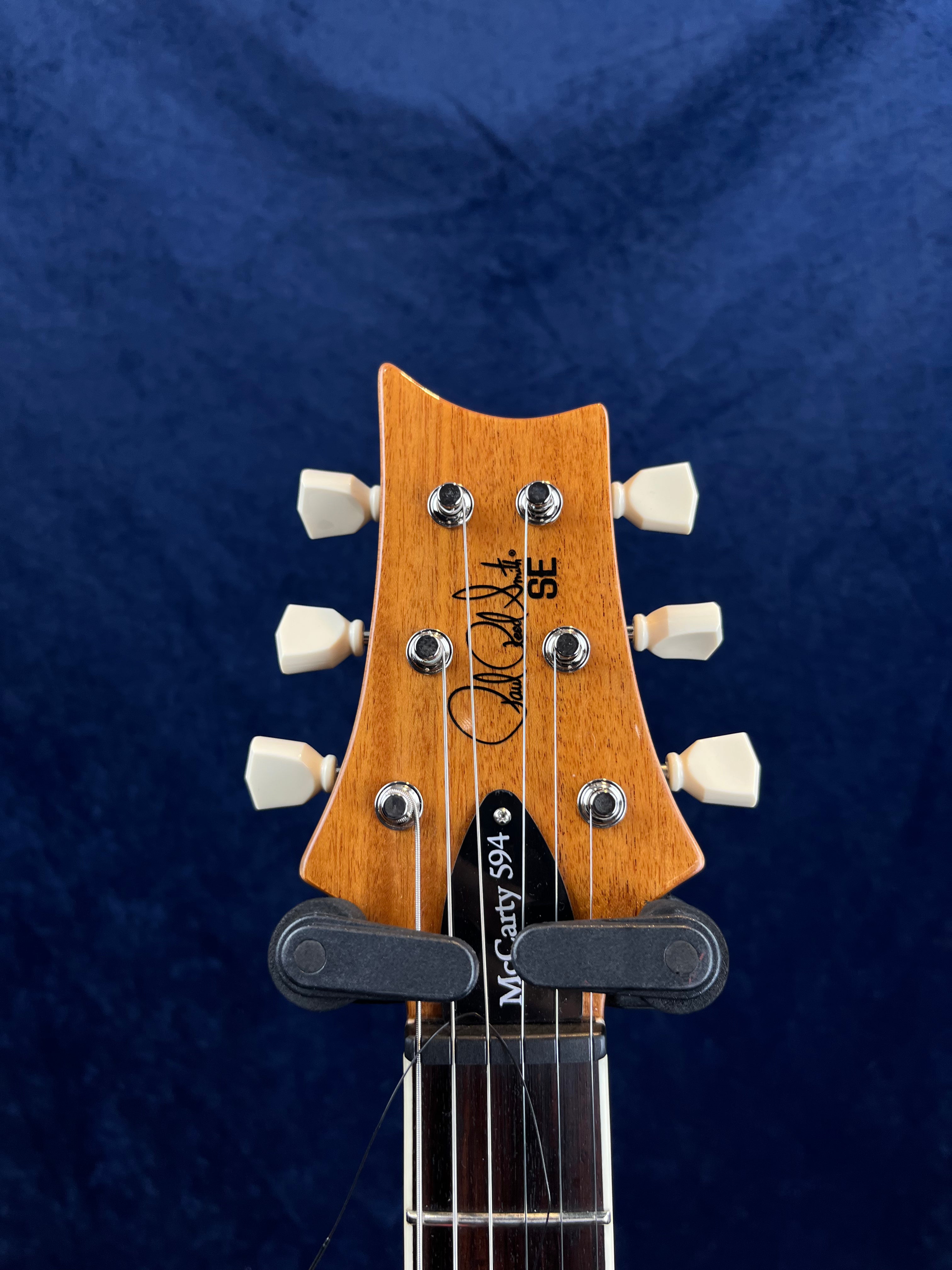 Tête de guitare électrique en bois verni, six mécaniques crème, logo Paul Reed Smith, inscription "SE" et "McCarty 594" sur une plaque noire.