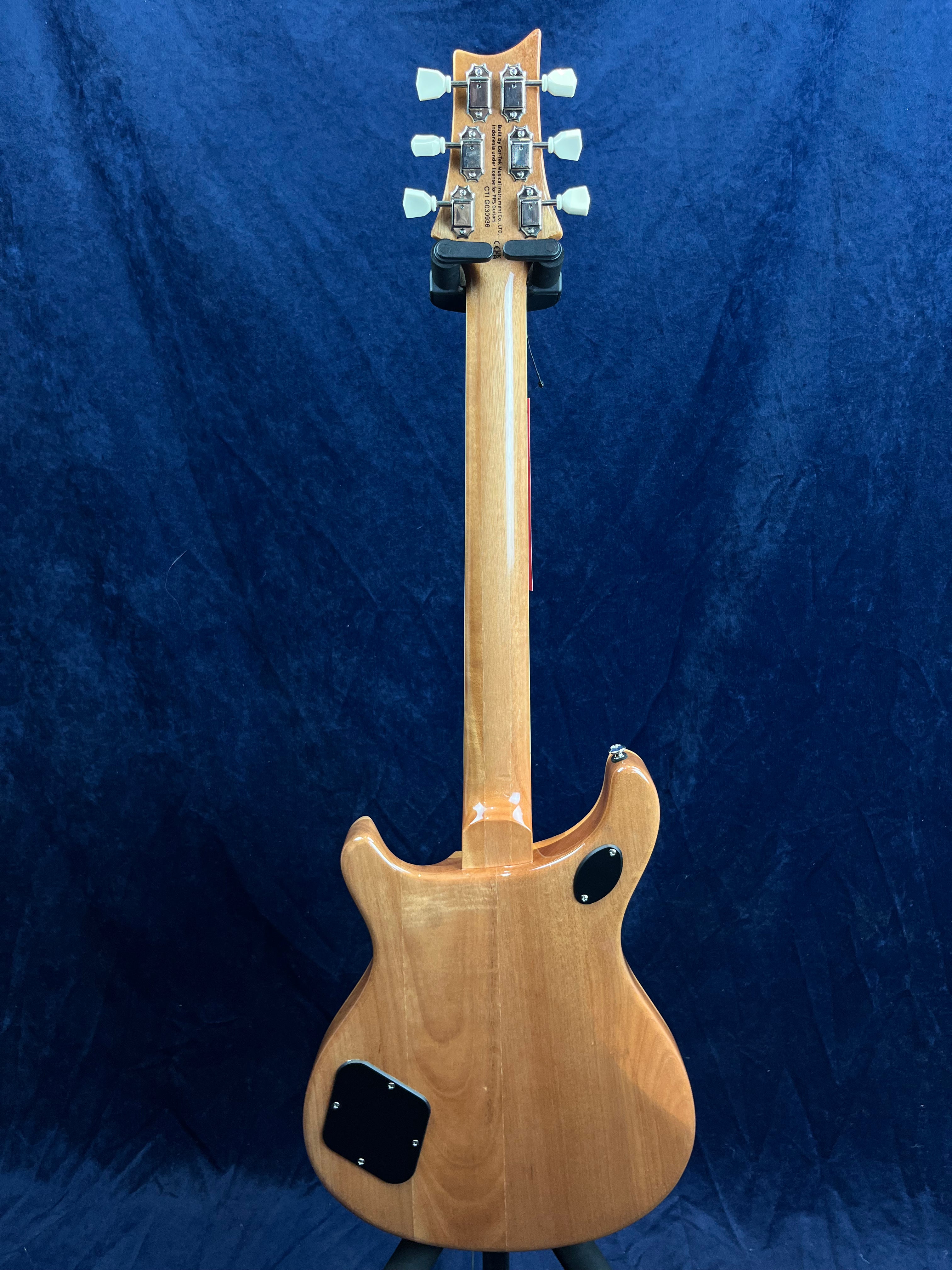 Guitare électrique en bois clair vue de dos, six mécaniques argentées avec boutons blancs, deux plaques d’accès noires sur le corps.