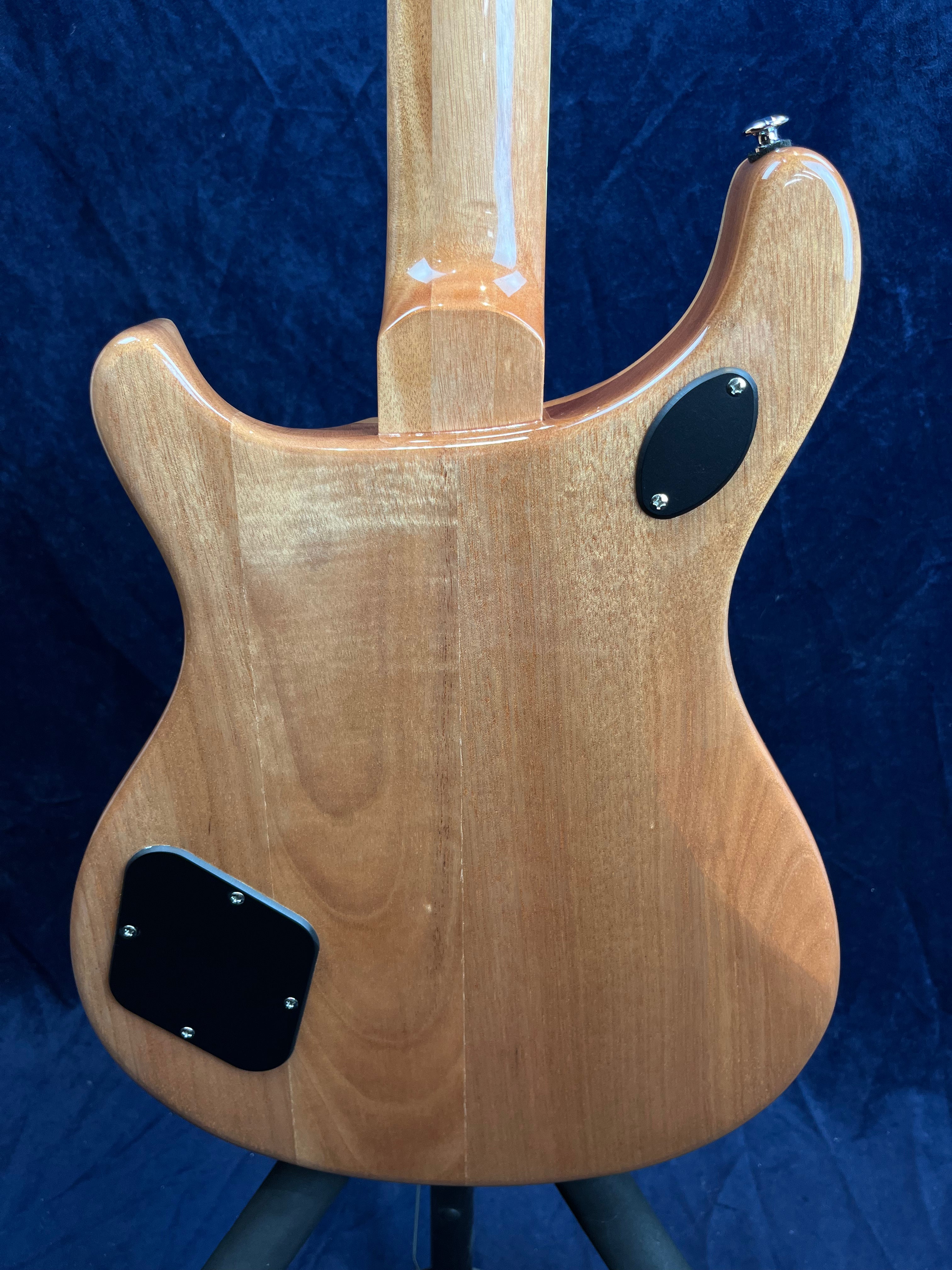 Corps d’une guitare électrique en bois naturel avec deux plaques noires vissées à l’arrière, sur fond bleu foncé.