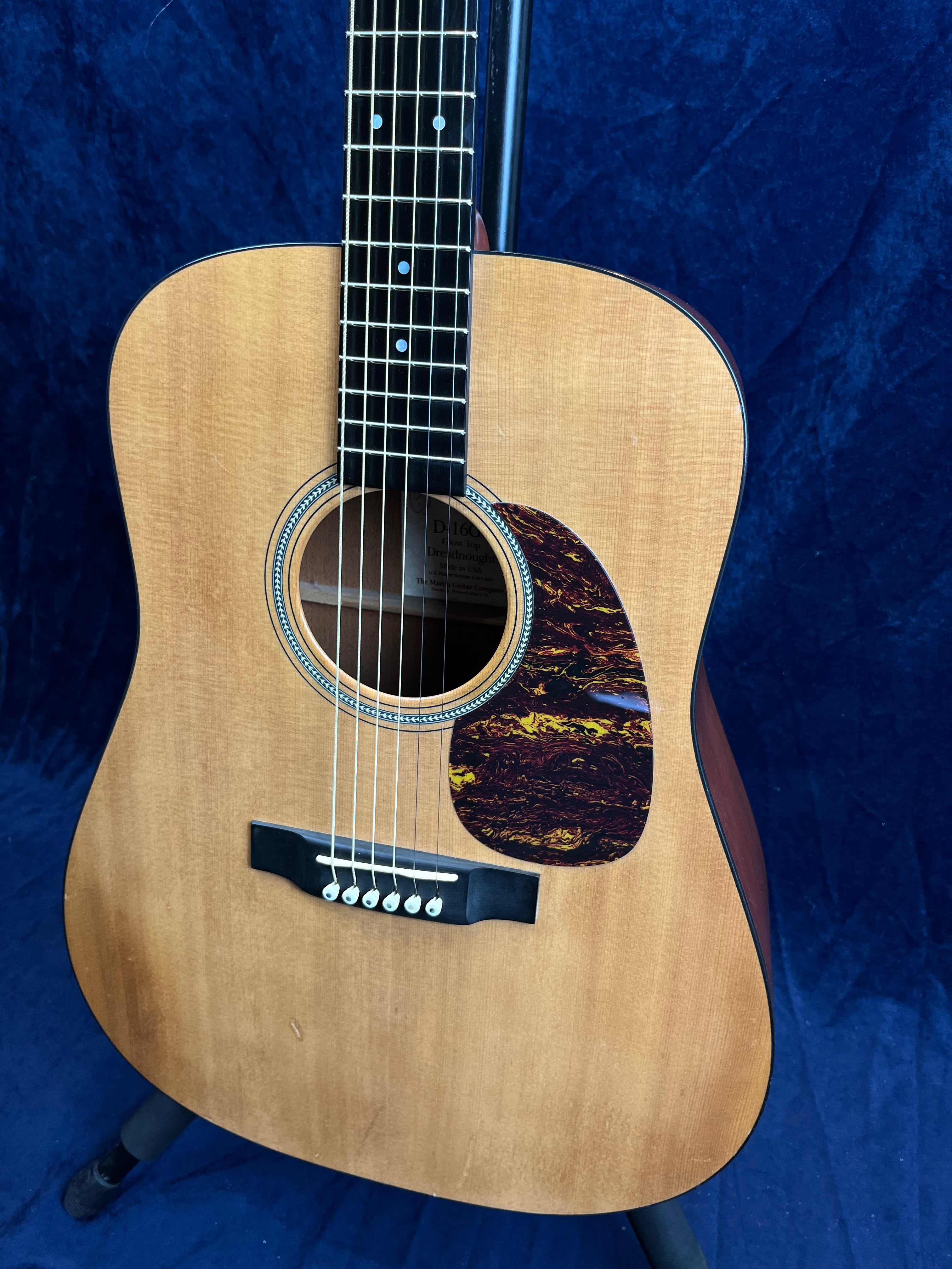 Natural wood acoustic guitar with a dark tortoiseshell pickguard, six strings, circular sound hole, and visible bridge pins.
