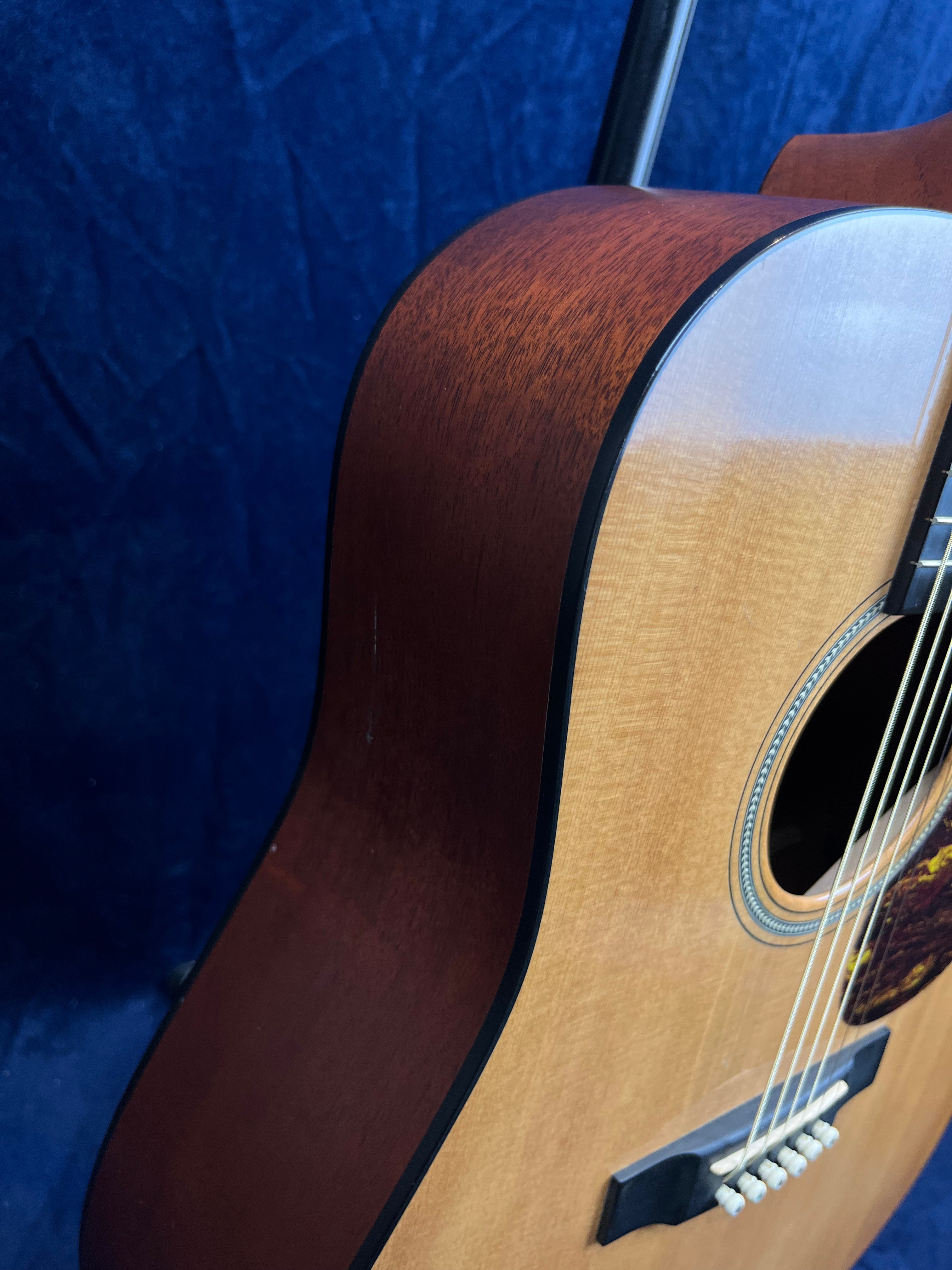 Acoustic guitar with a light-colored top, darker wood sides, and visible sound hole against a dark blue background.