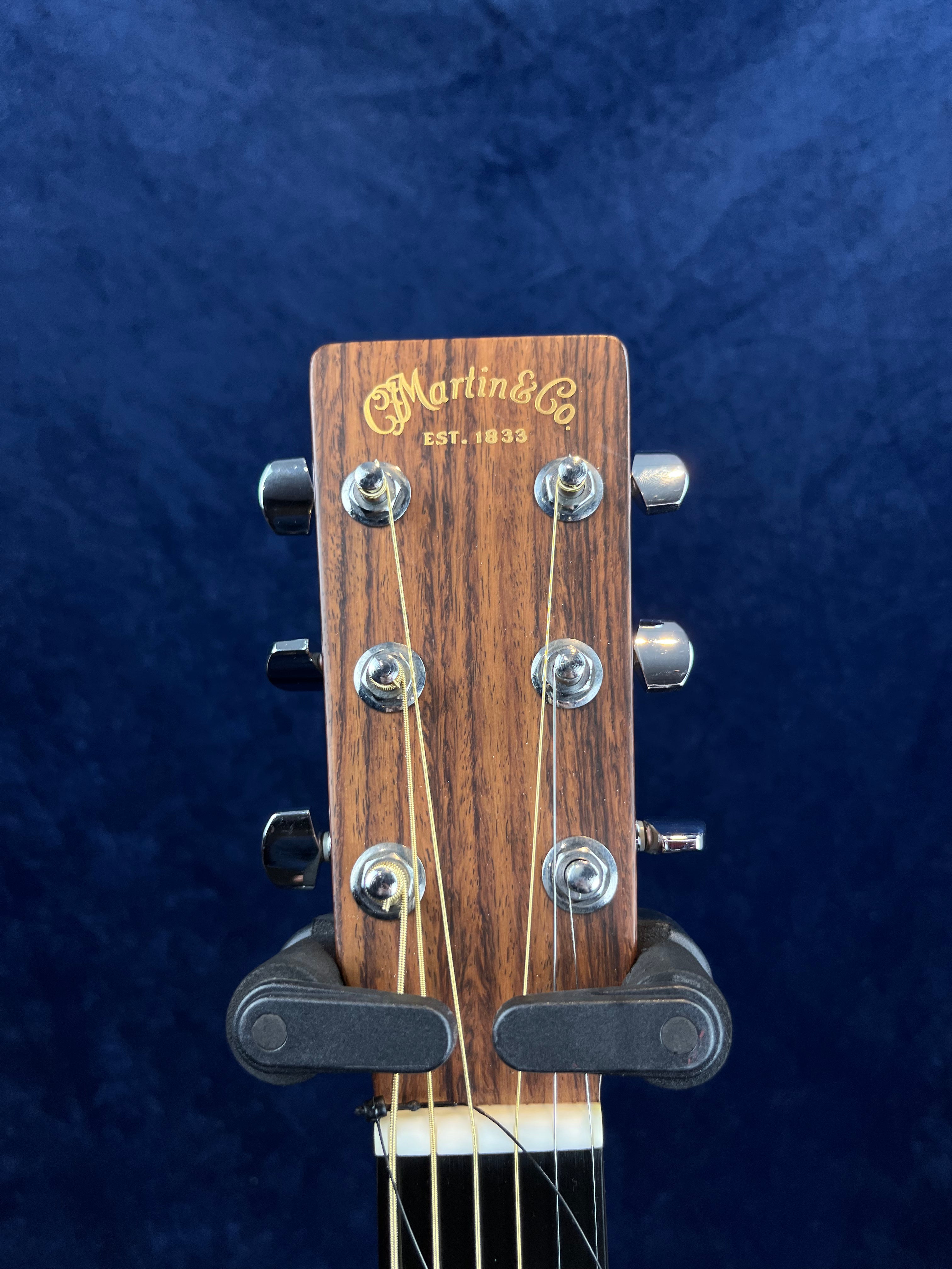 Close-up of a Martin & Co acoustic guitar headstock with six tuning pegs against a dark blue background.