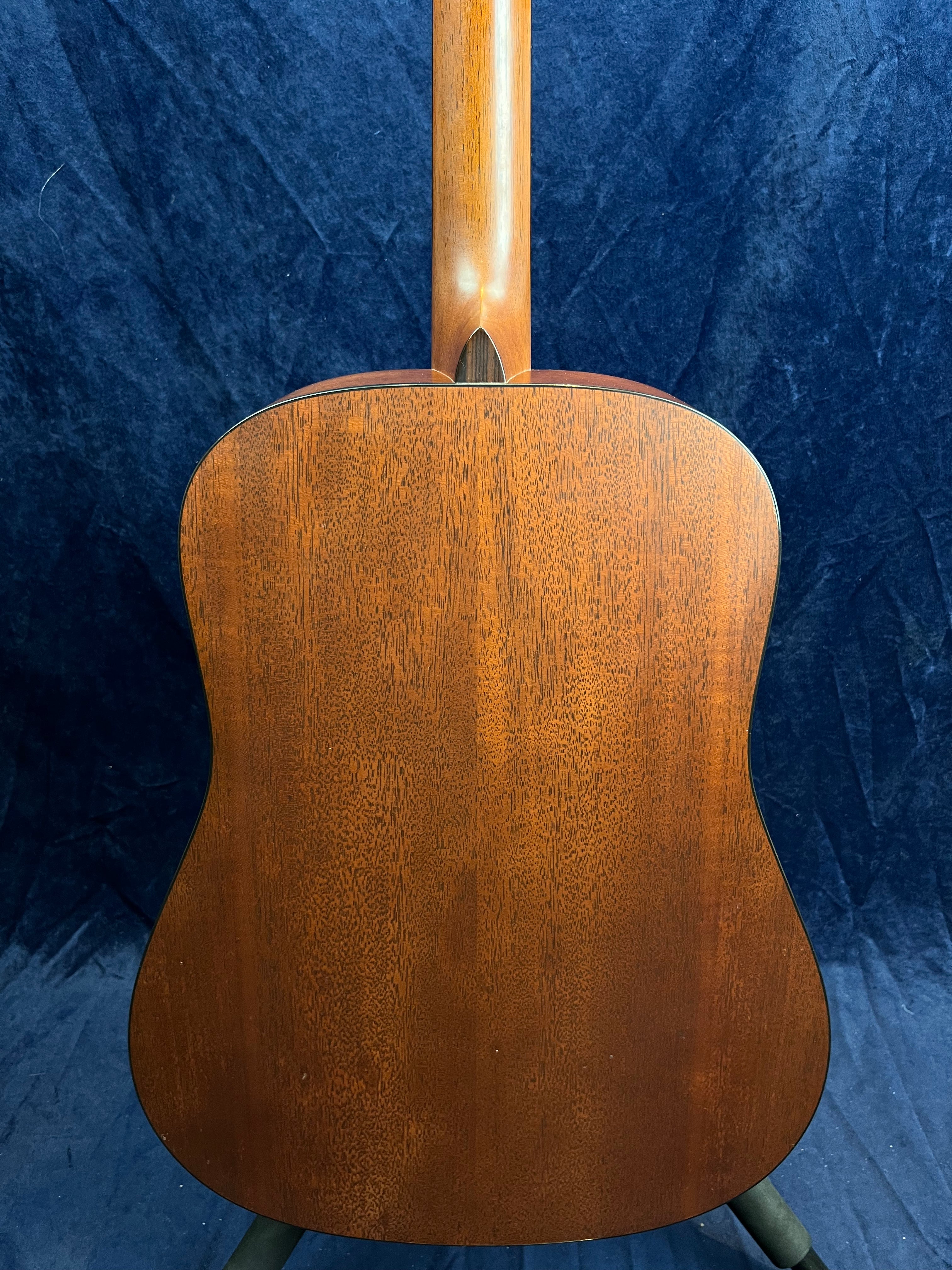 Back view of an acoustic guitar with a smooth, rich brown wooden finish and visible natural wood grain patterns.