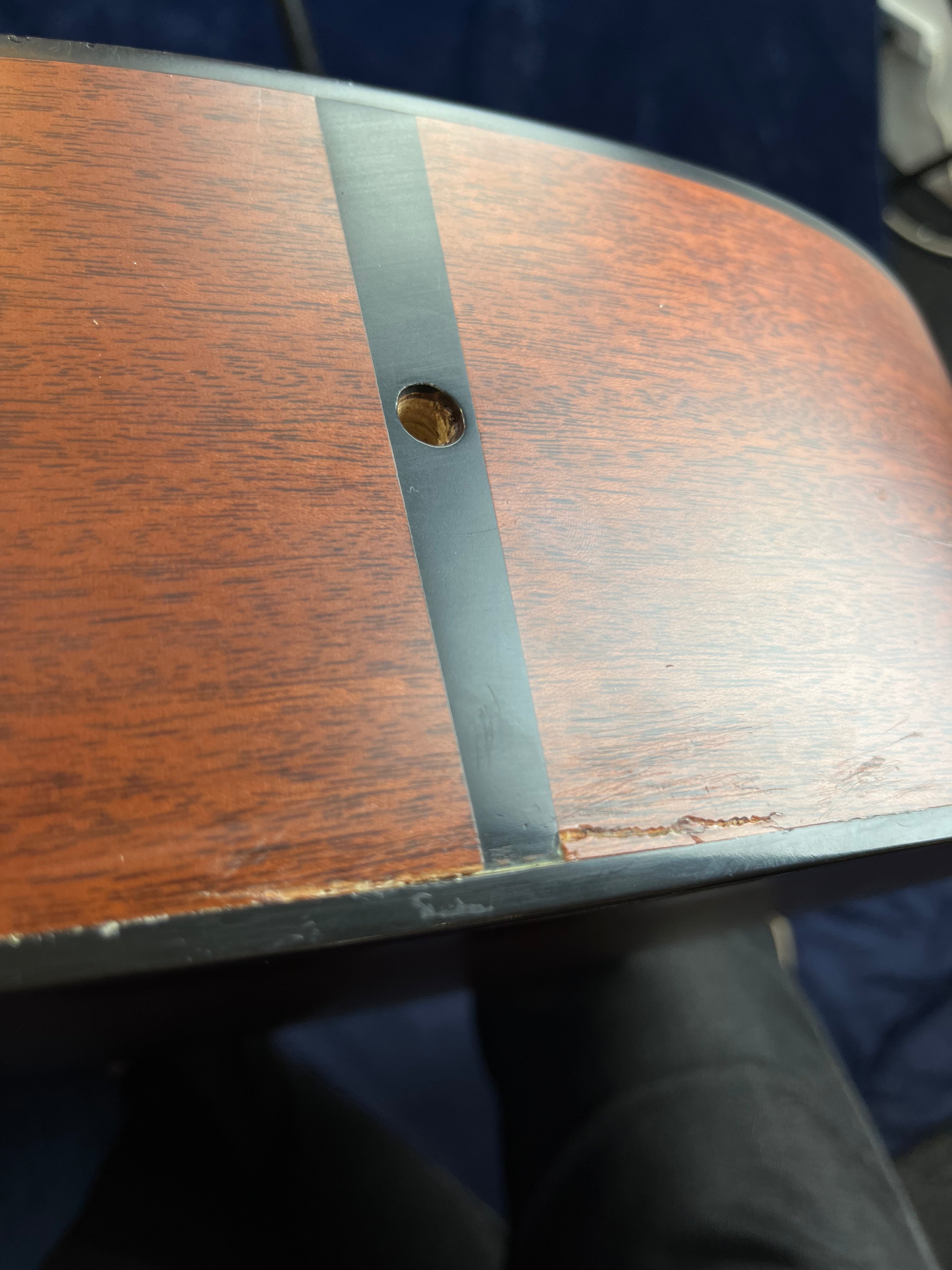 Acoustic guitar side showing a circular hole for a strap button and a long scratch or crack along the edge of the wood grain.