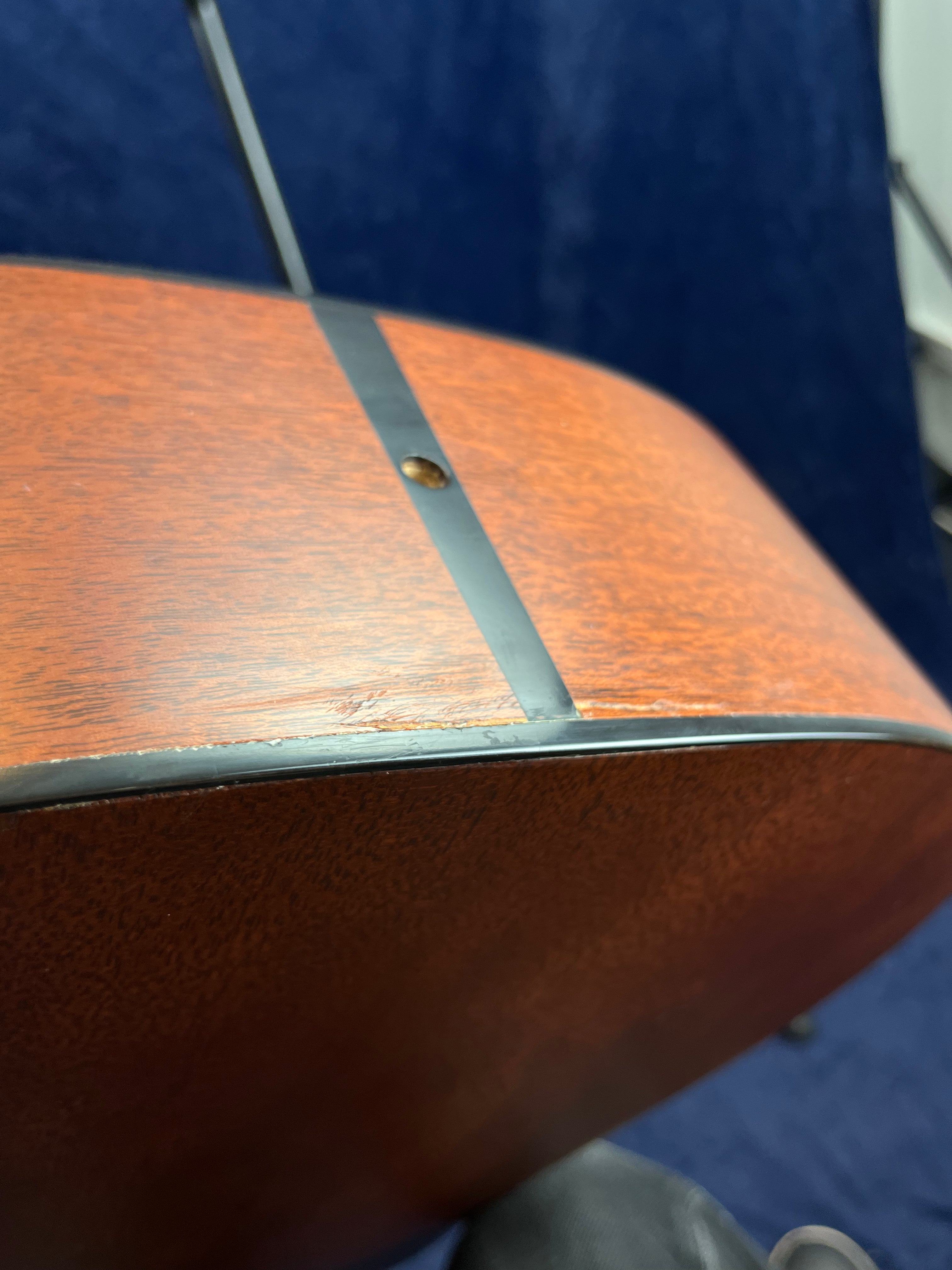 Acoustic guitar side with a visible scratch and a small dent near the black binding and strap button hole.