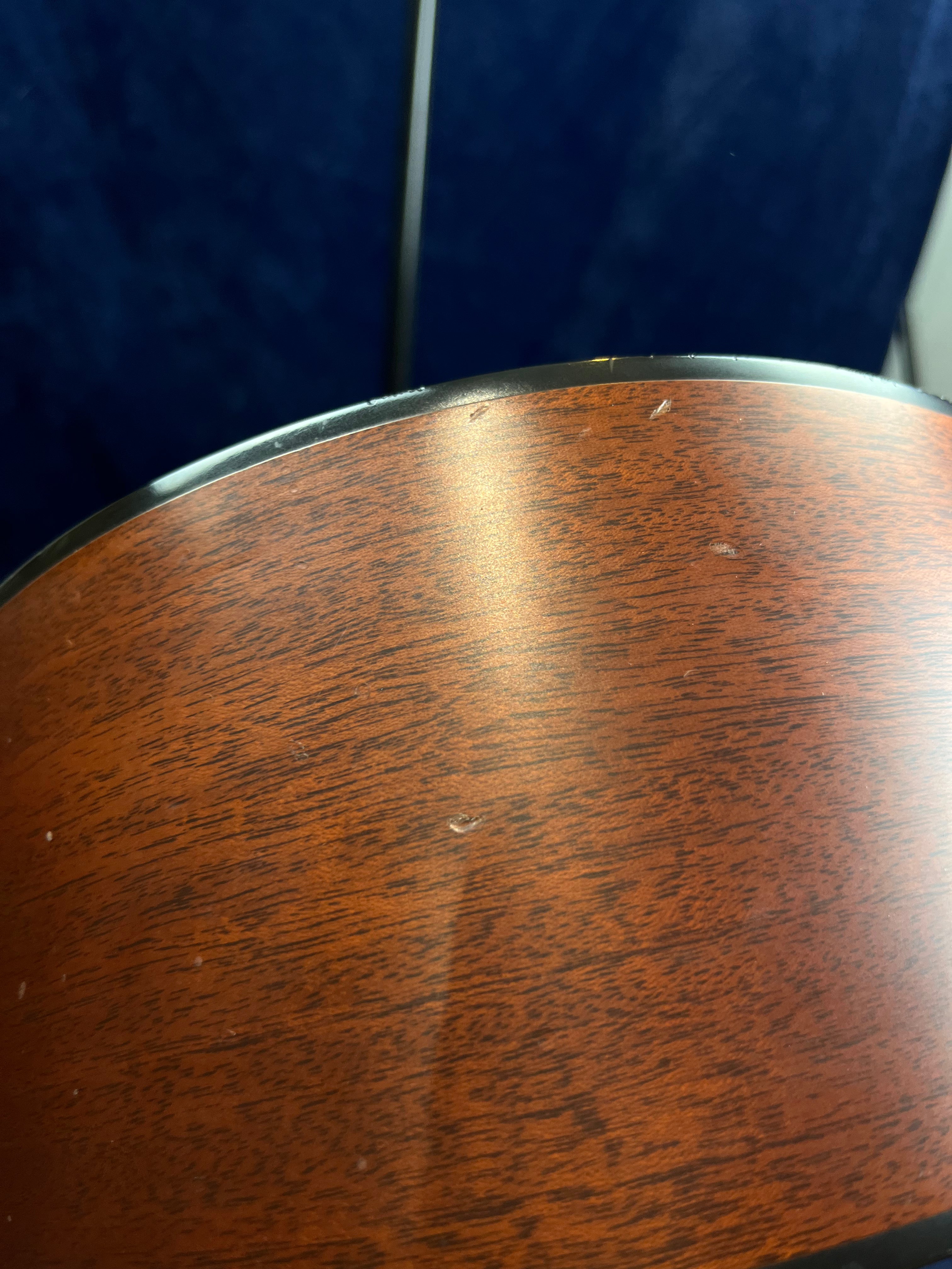 Light scratches and small dents are visible on the polished wooden side of an acoustic guitar, with black binding along the edge.