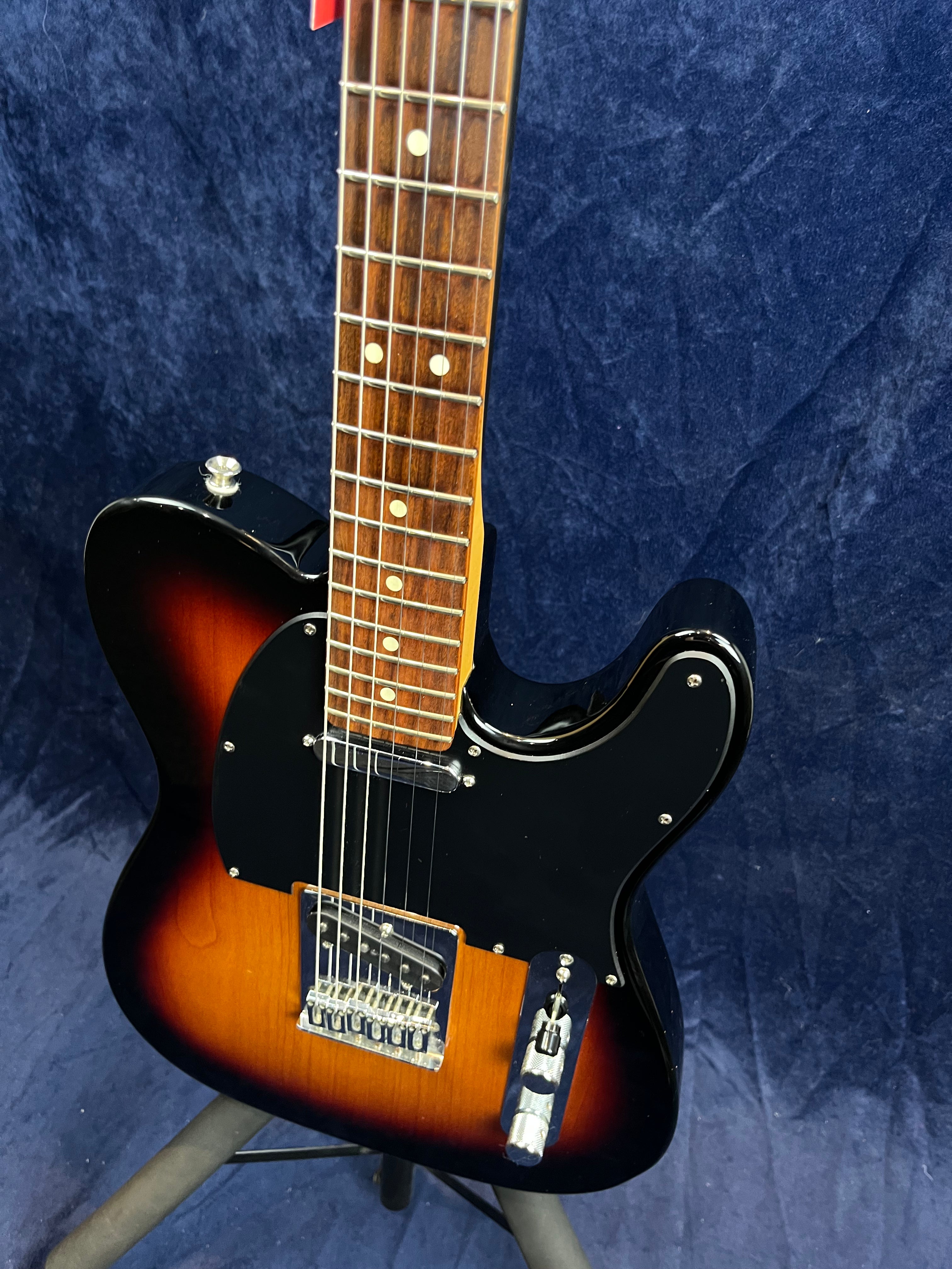 Guitare électrique à corps marron sunburst, plaque noire, deux micros, manche et touche en bois foncé, posée sur un support.