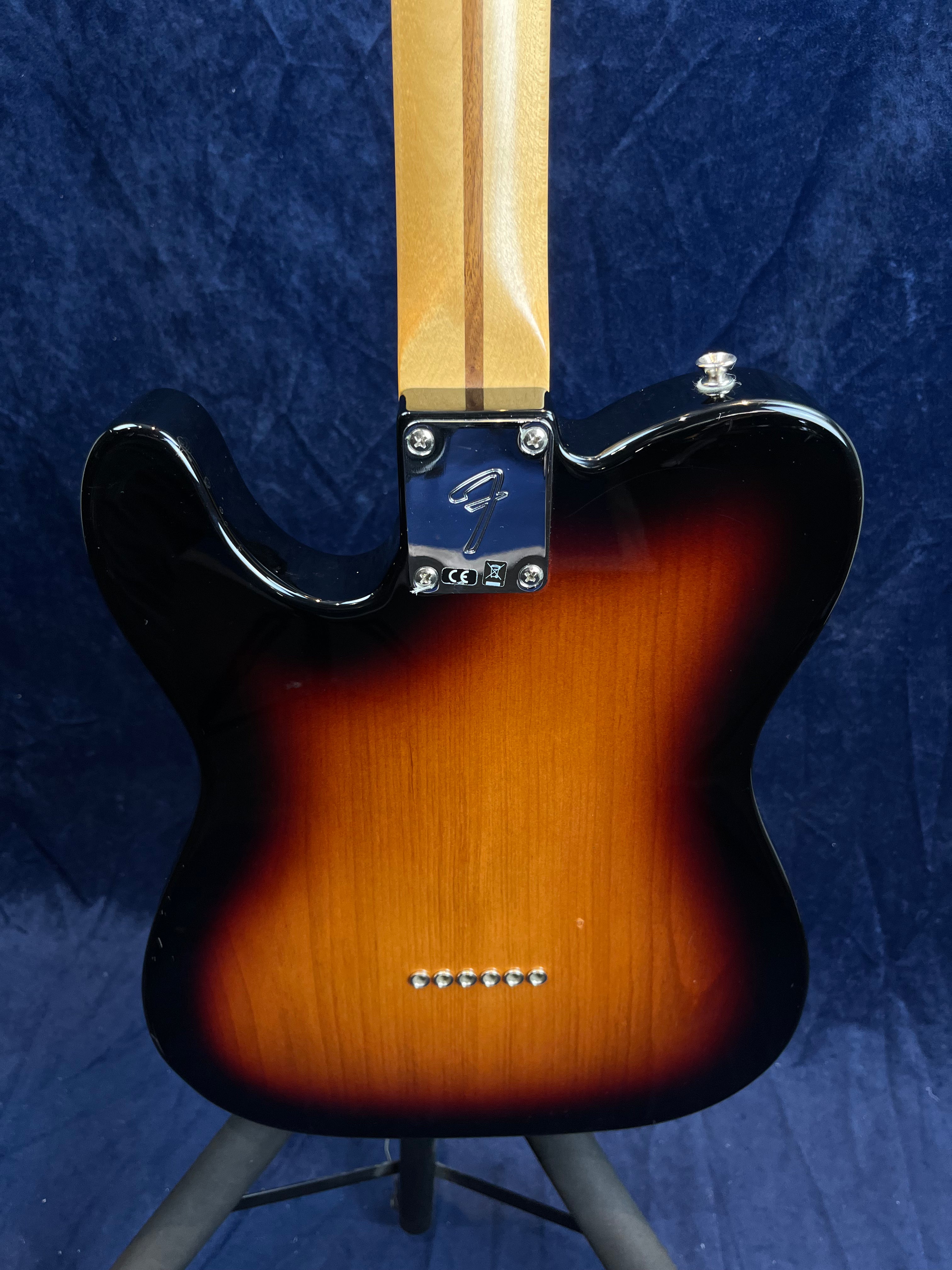 Corps de guitare électrique sunburst, dos en bois verni avec six axes chromés alignés et plaque métallique fixant le manche, fond bleu foncé.