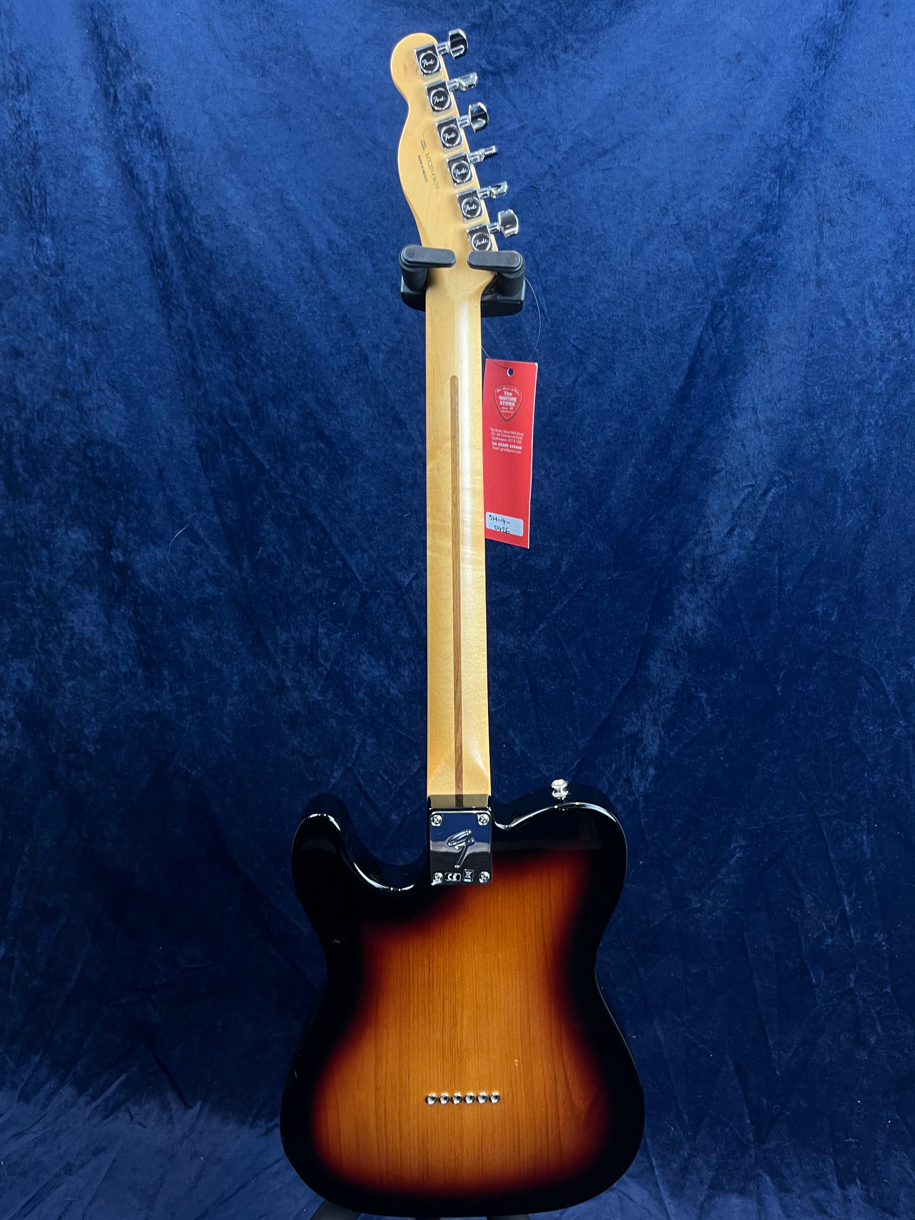 Guitare électrique sunburst vue de dos, manche en érable clair, six mécaniques argentées, étiquette rouge accrochée à la tête.