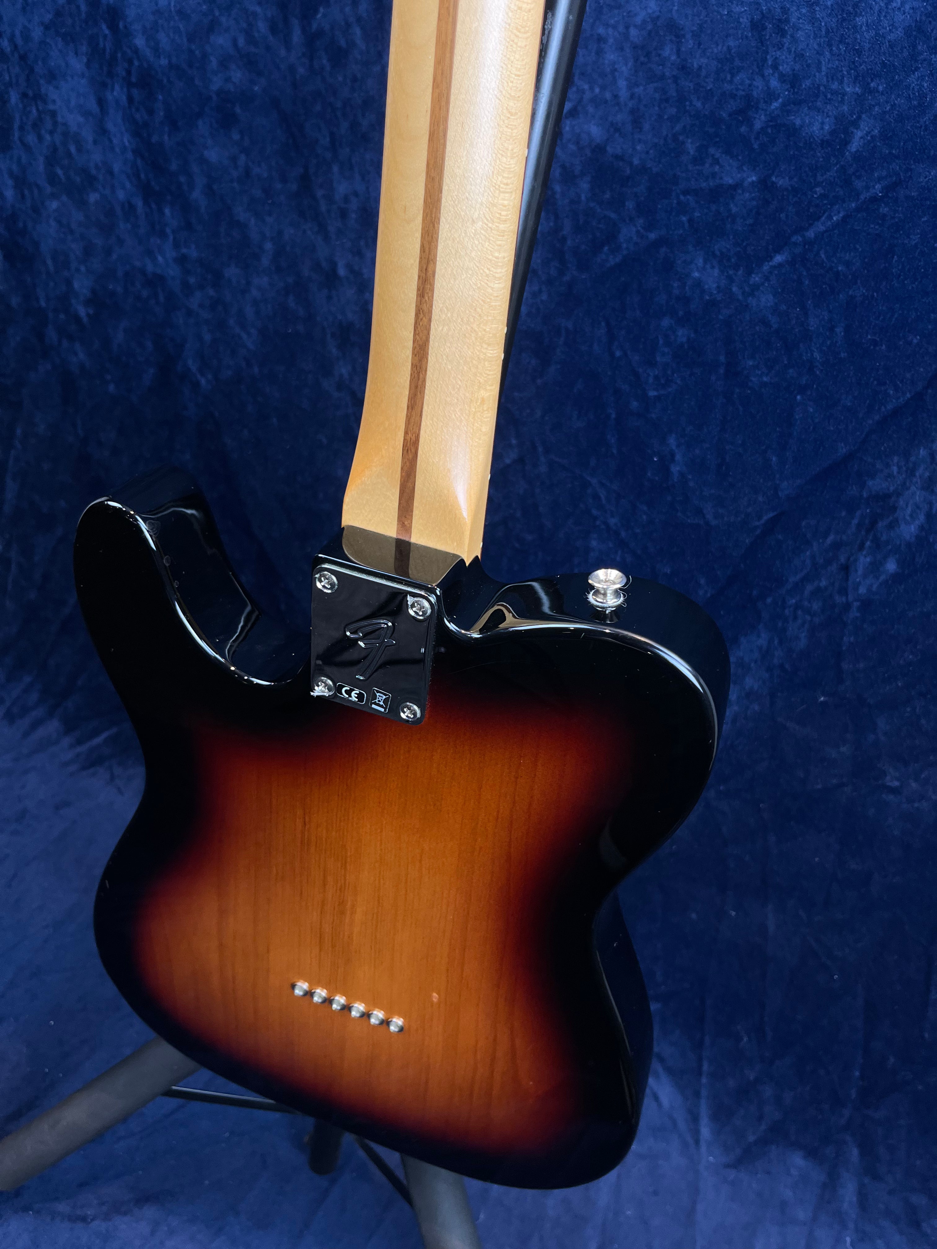 Guitare électrique avec corps marron sunburst, dos visible, manche en érable clair traversé d'une bande foncée, fond bleu.