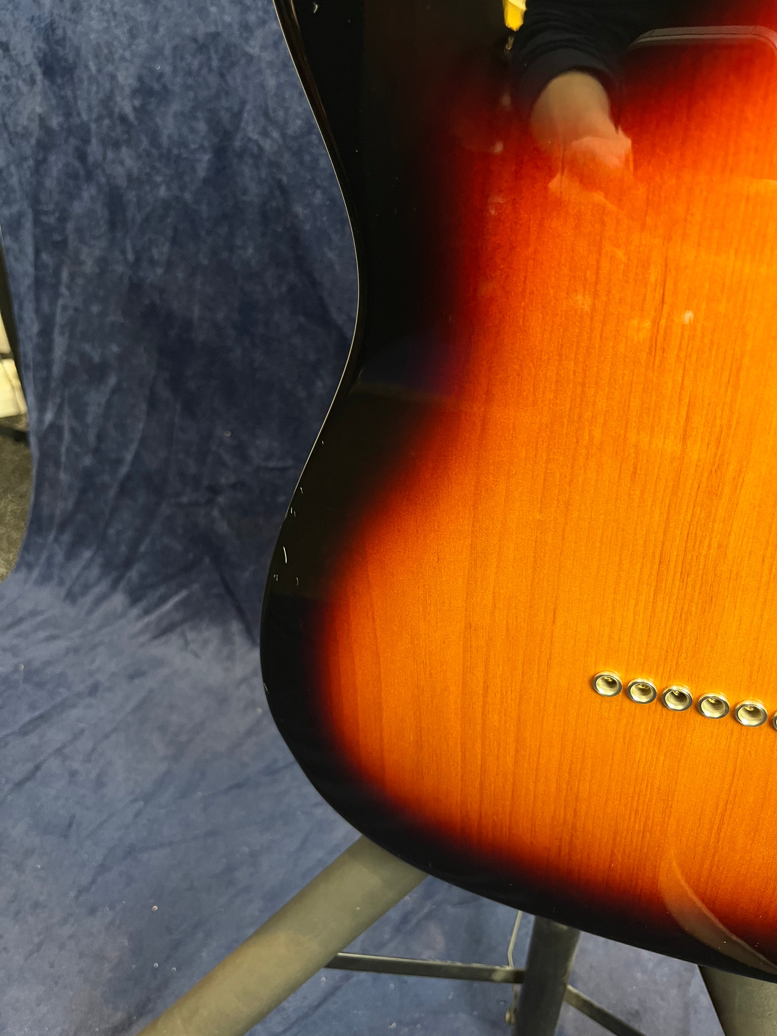 Partie arrière d’une guitare électrique finition sunburst, avec six œillets métalliques alignés pour le passage des cordes.