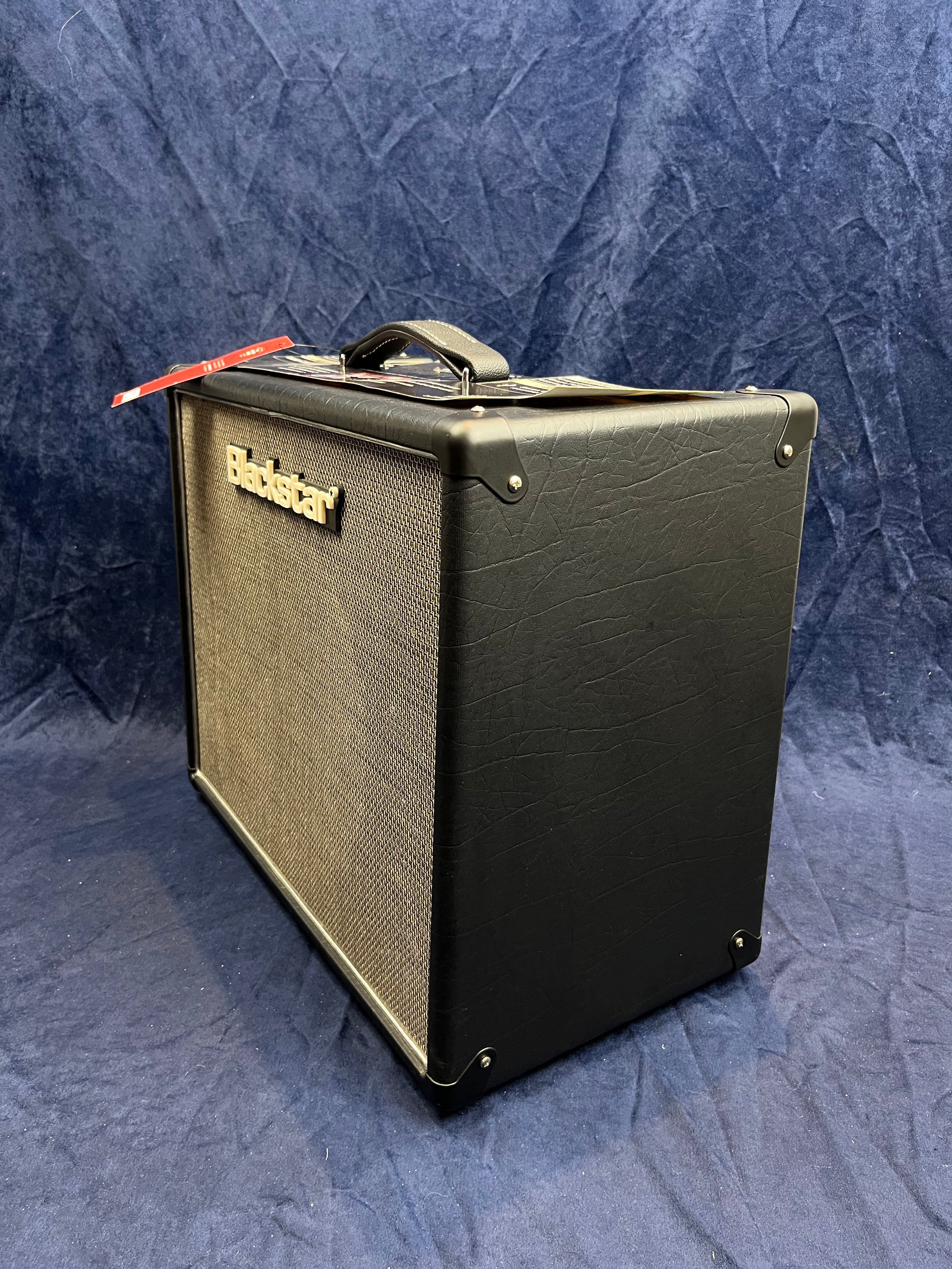 Blackstar guitar amplifier with a textured black finish, mesh front grill, and a handle on top. A red tag is attached to the handle.