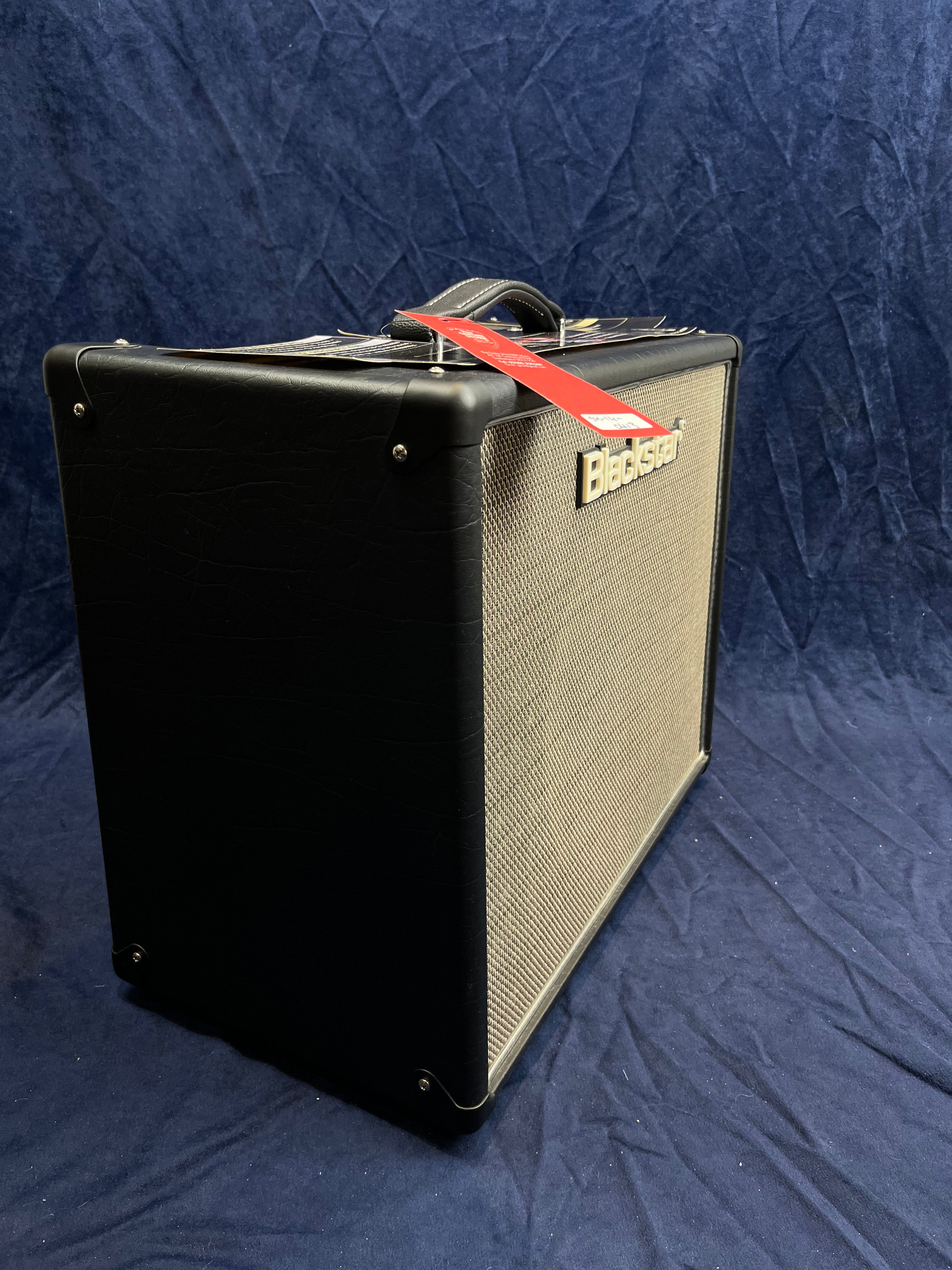 Blackstar guitar amplifier with a textured black exterior, silver mesh front, carrying handle on top, and a red product tag attached.
