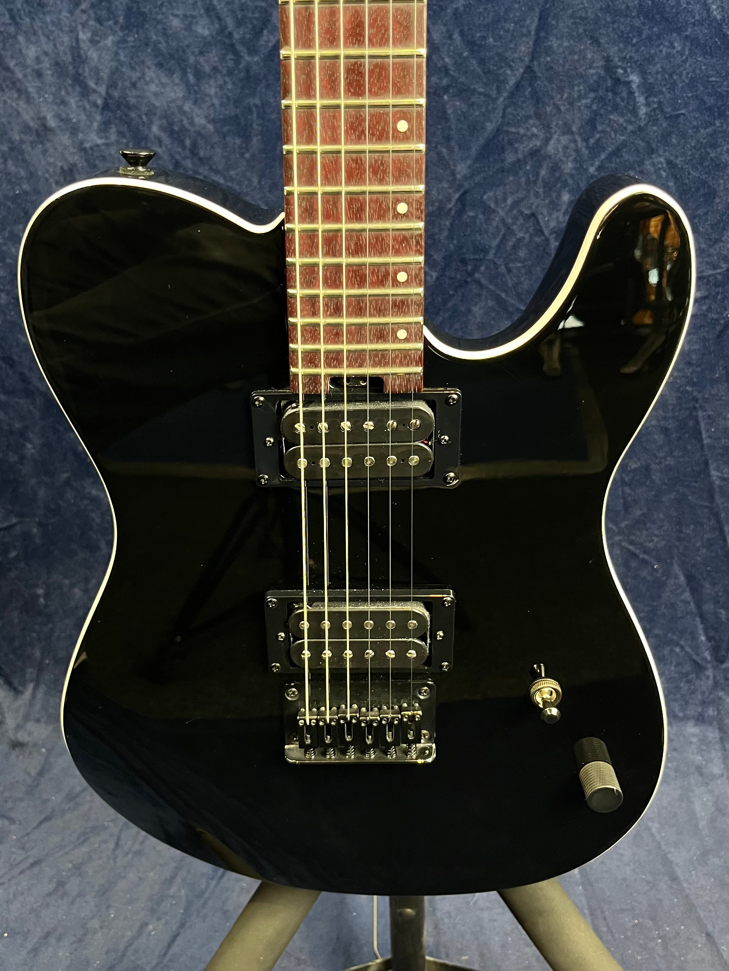 Glossy black electric guitar with a single cutaway, two humbucker pickups, a selector switch, and one large control knob on the body.