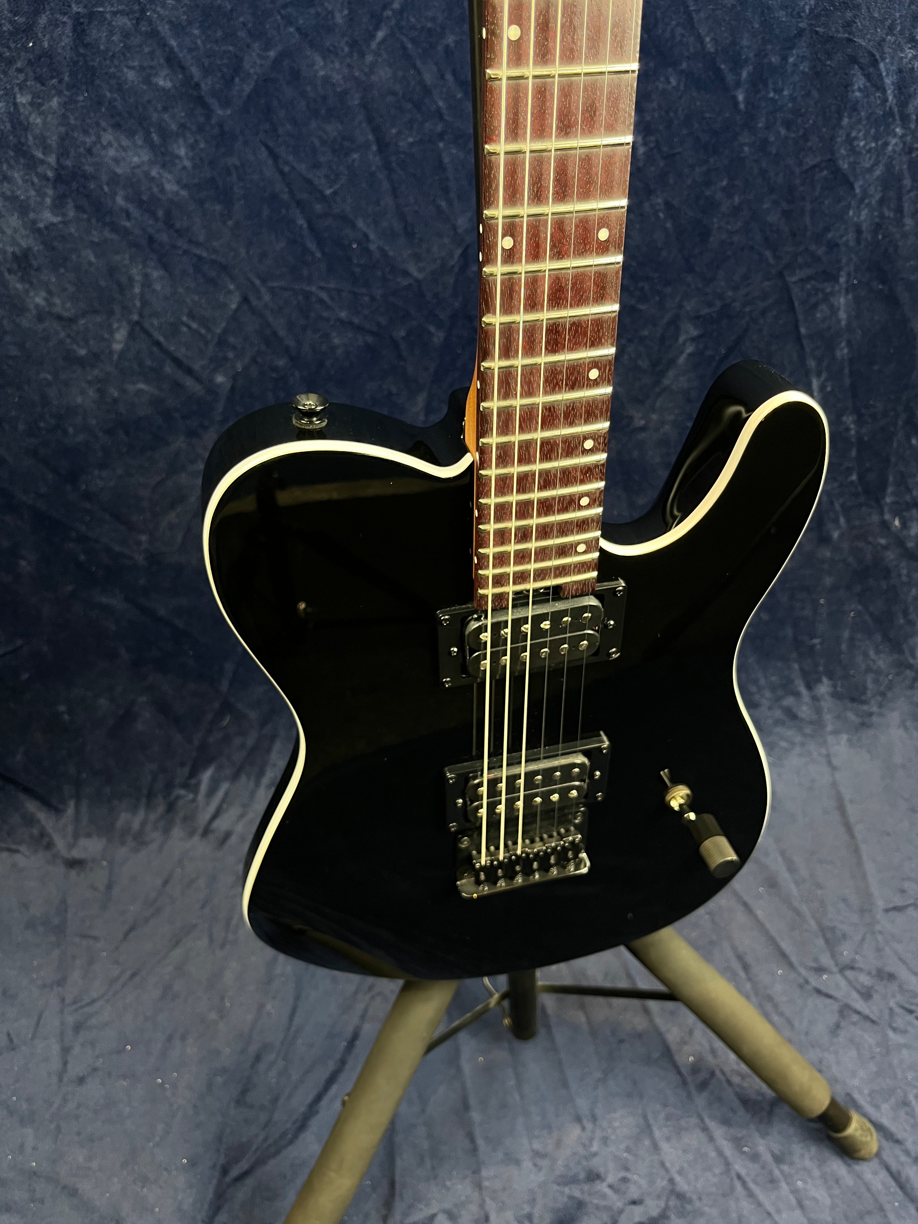 Glossy black electric guitar with a double humbucker pickup configuration, white trim, and a tremolo bridge, displayed on a stand against a dark background.