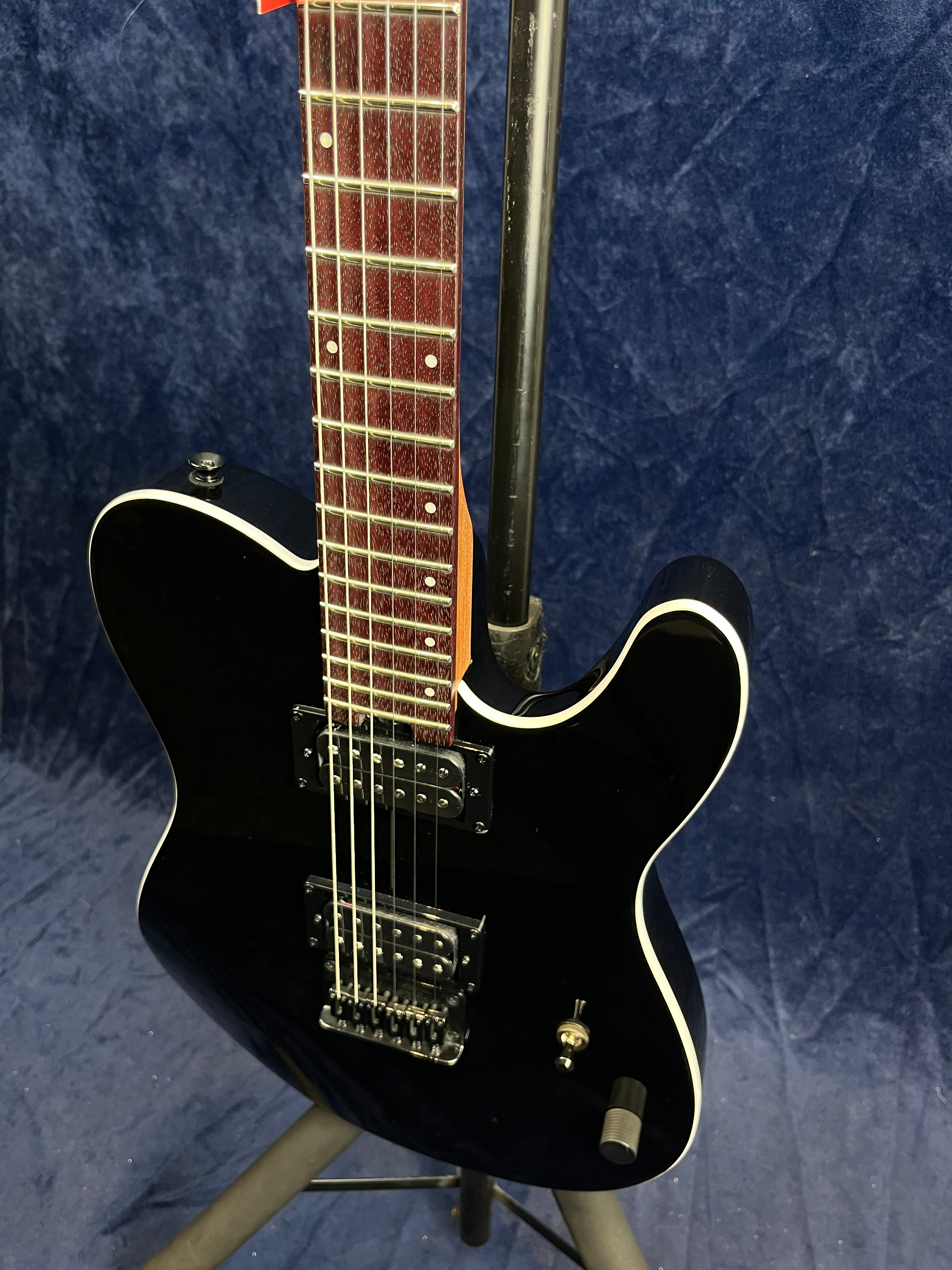 Black electric guitar with a glossy finish, white body binding, two humbucker pickups, and a rosewood fretboard on a stand against a blue background.