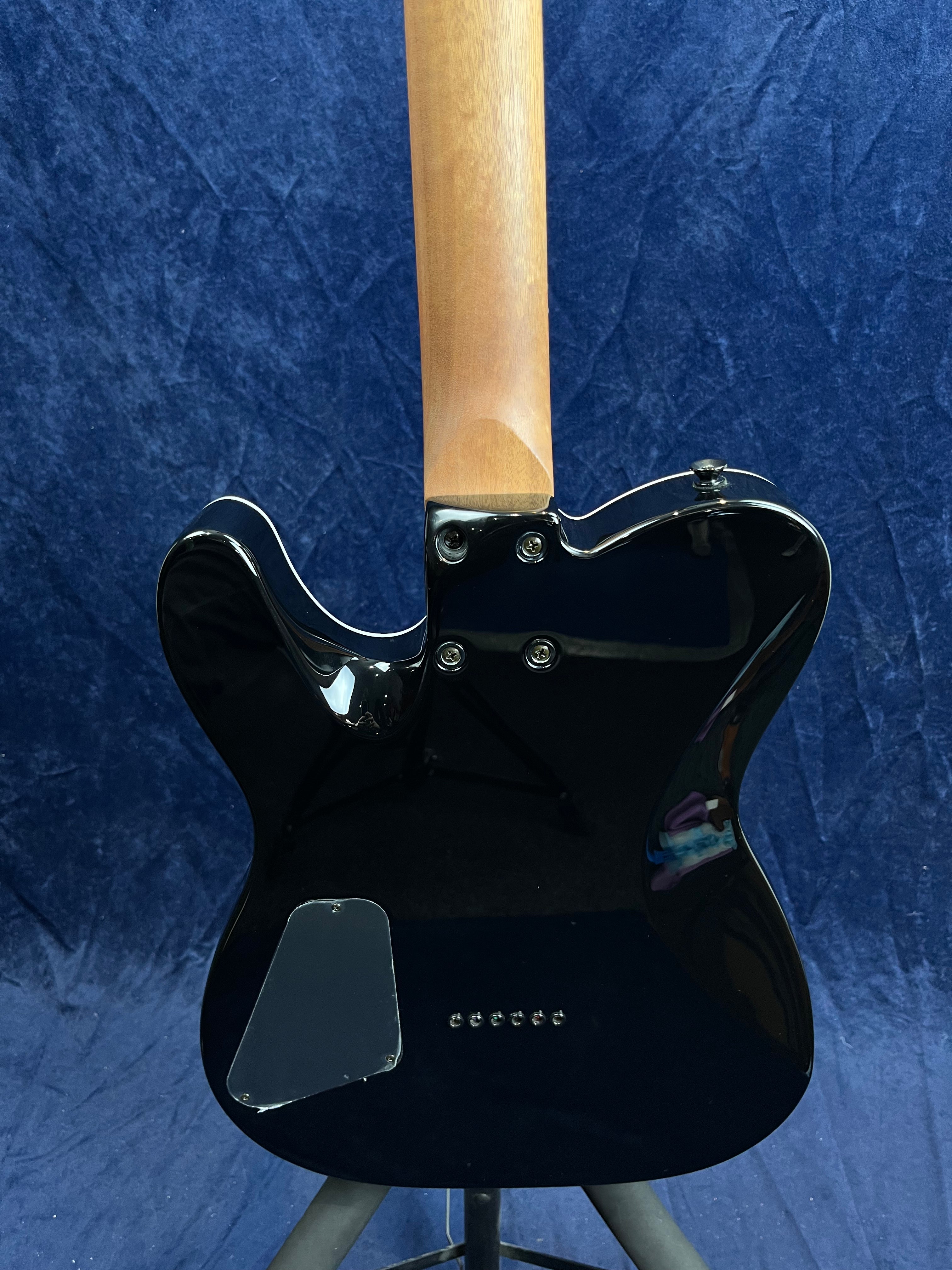 Electric guitar rear view showing a glossy black body, exposed natural wood neck, and a plastic electronics cover on the lower left side.