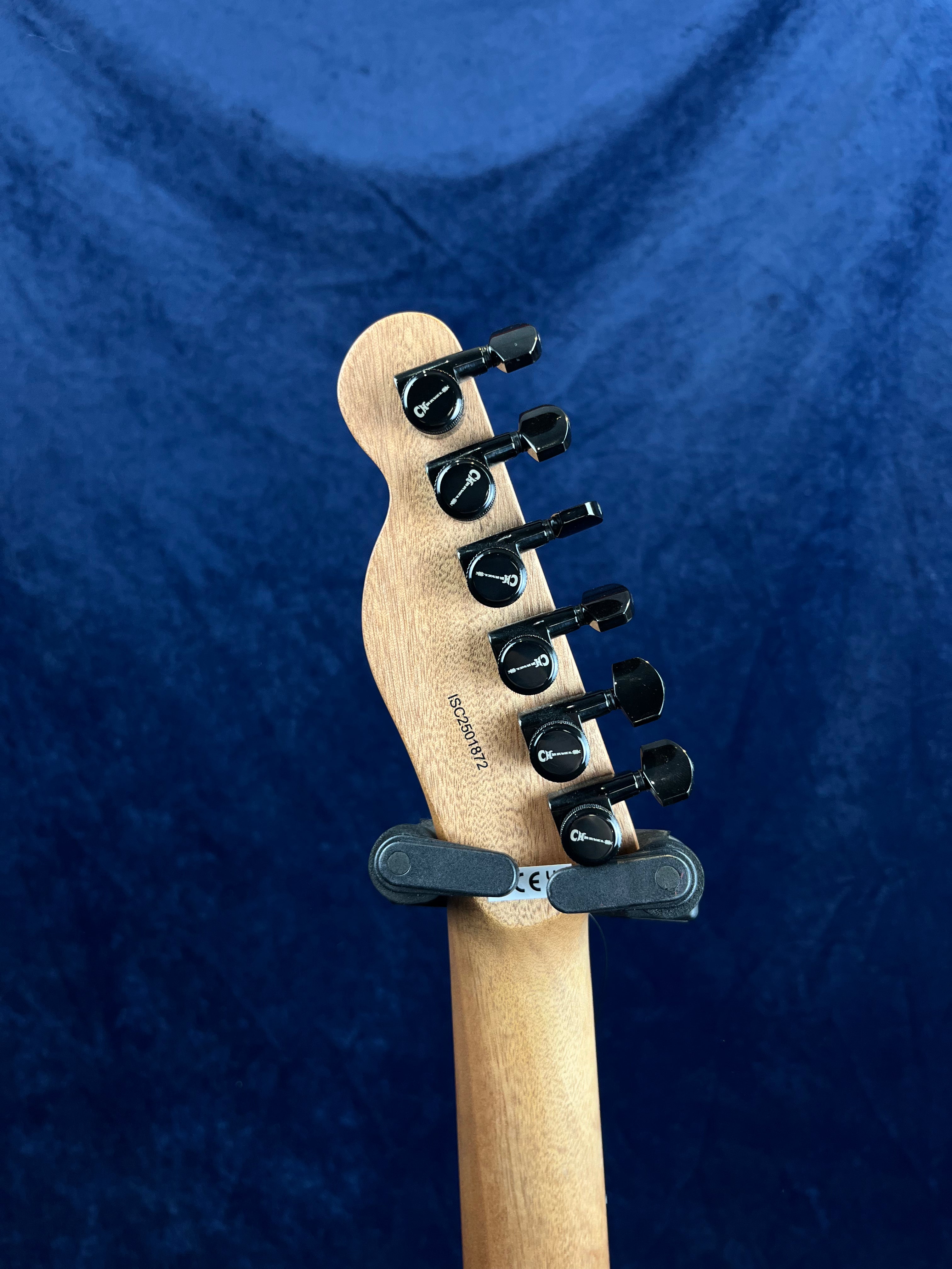 Wooden electric guitar headstock with six black tuning pegs is shown against a blue background, held upright by a hanger.