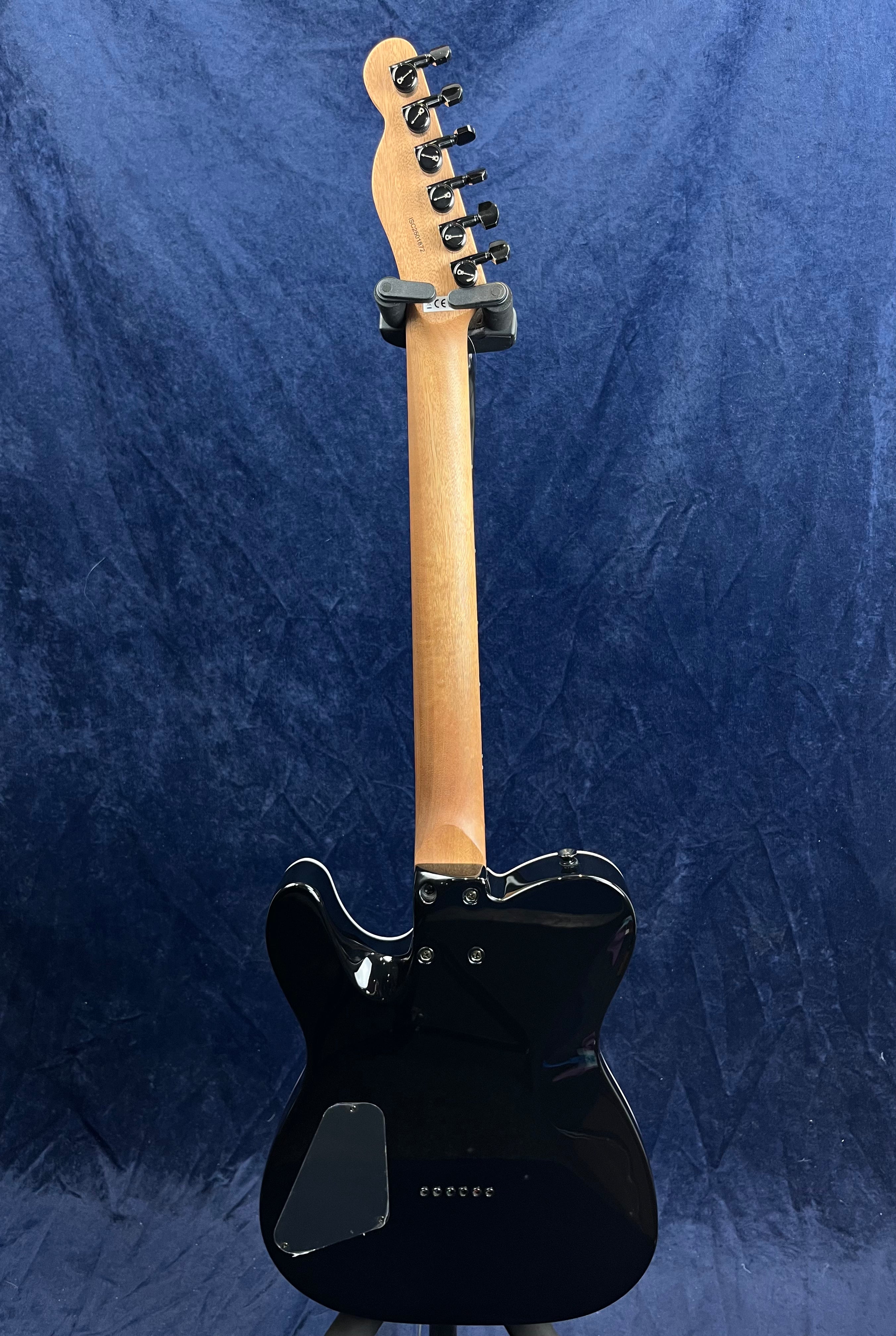 Black electric guitar seen from the back, showing a wooden neck with six tuning pegs and a glossy black contoured body against a dark blue background.