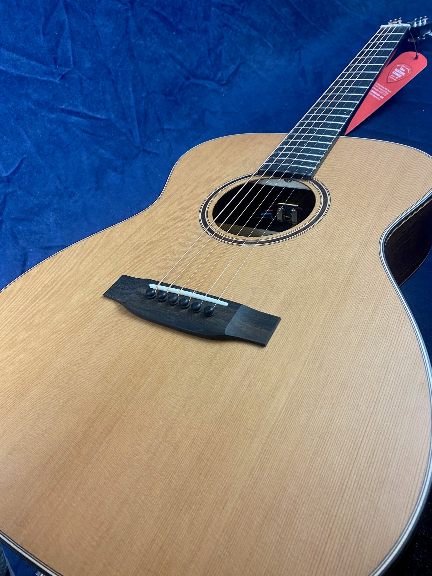 Light wood acoustic guitar with a dark bridge and fretboard, round sound hole, and a red tag hanging from the headstock.
