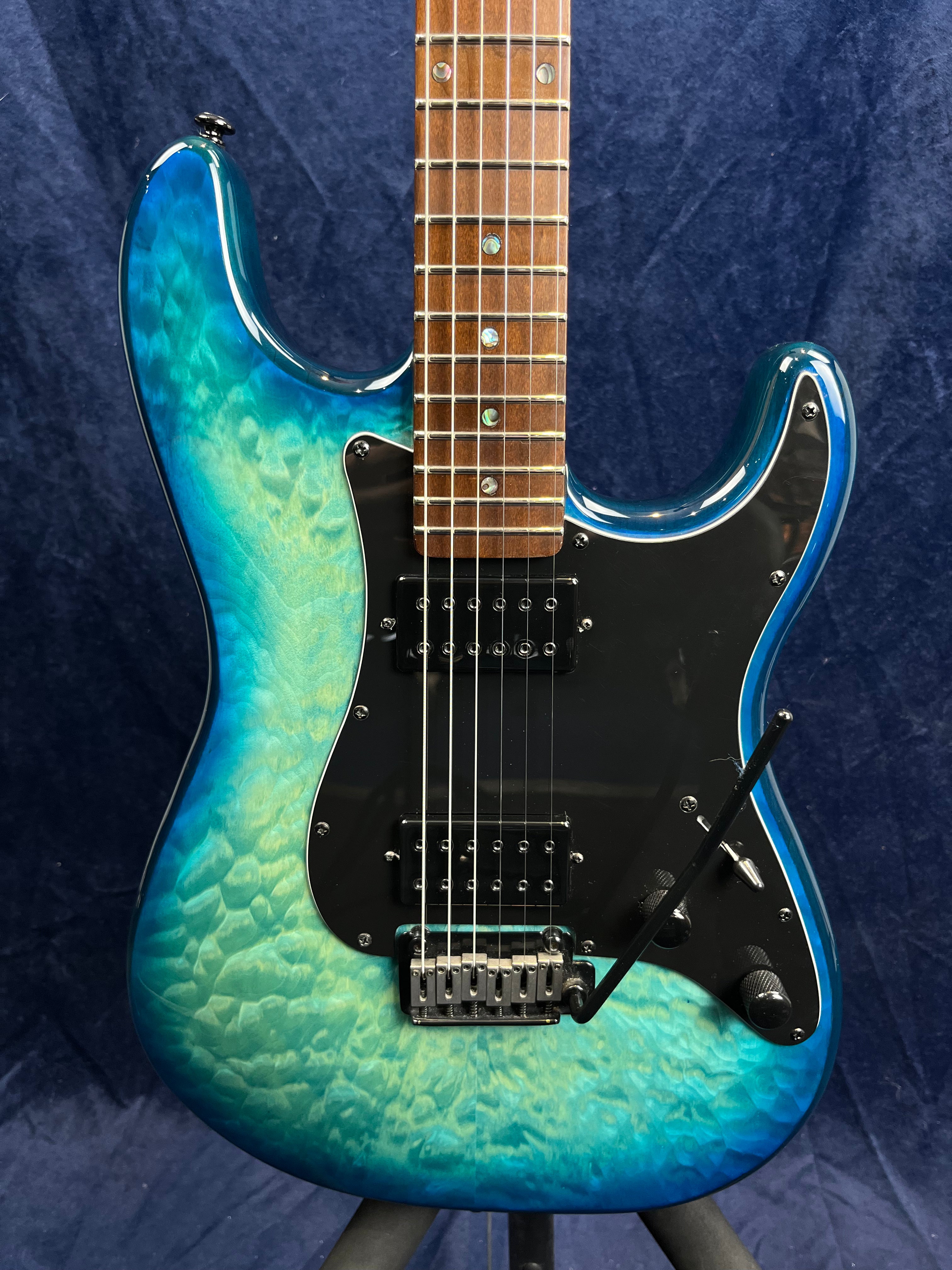 Electric guitar with a blue-to-green quilted finish, black pickguard, two humbucker pickups, whammy bar, and rosewood fretboard.