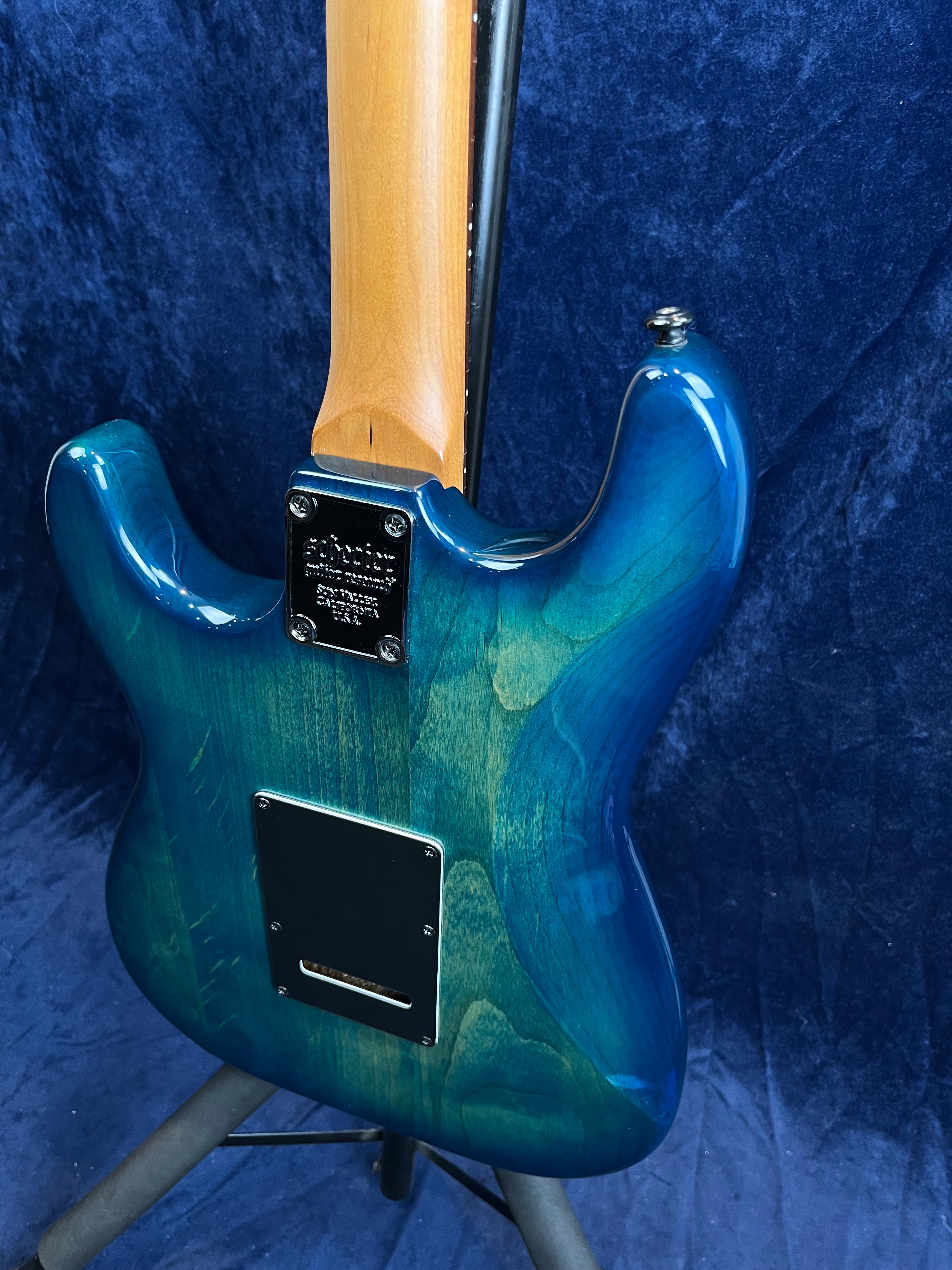 Blue-green electric guitar shown from the back, with a wooden neck, two black access plates, and glossy finish on the contoured body.