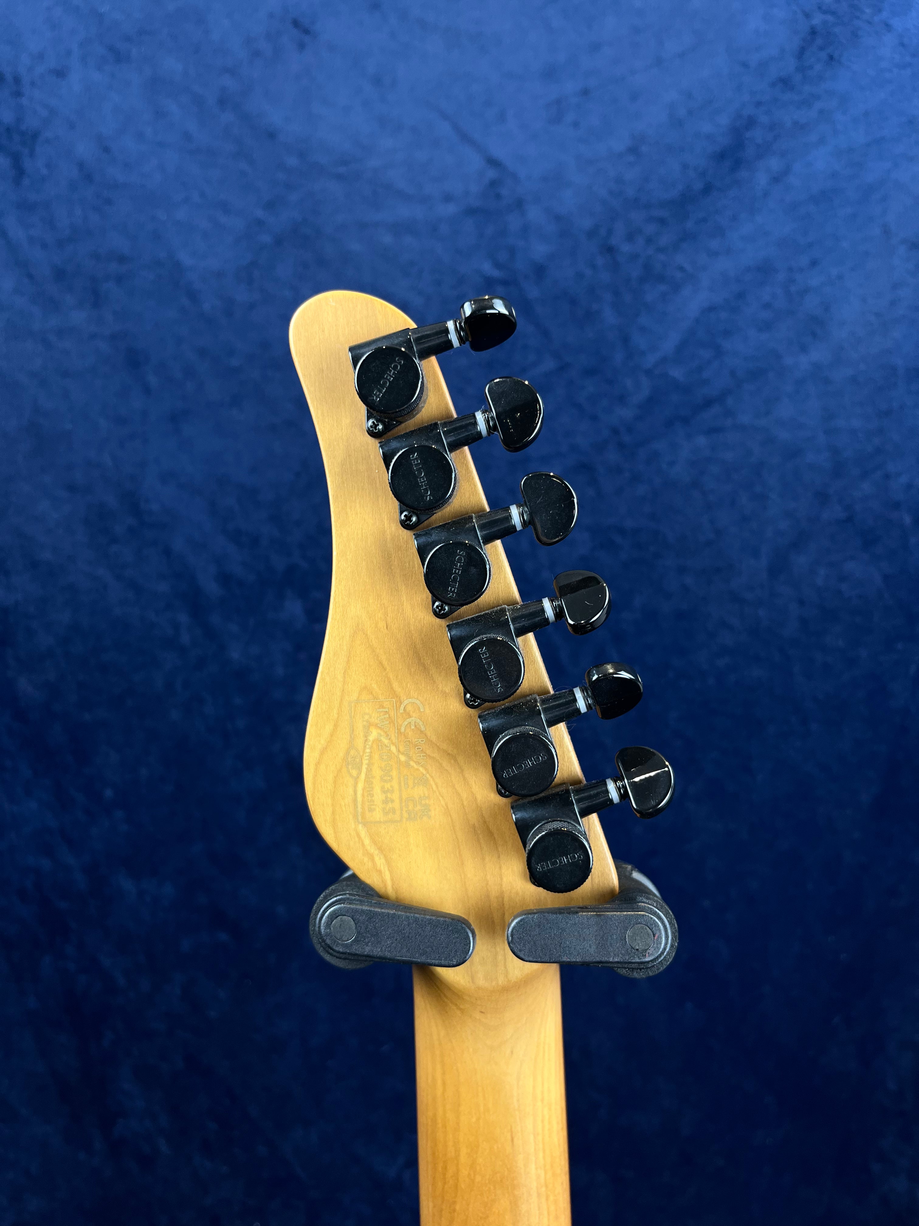 Six black tuning pegs on the back of a light wood electric guitar headstock, held in a wall-mounted guitar hanger against a dark blue background.